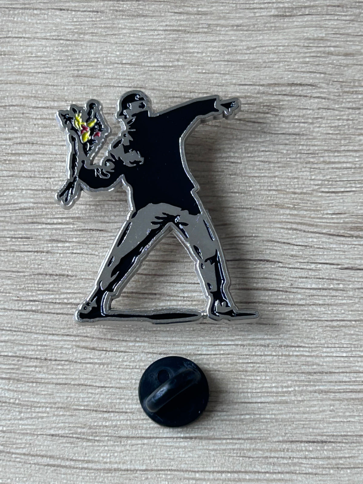 Broche lanceur de fleurs, silhouette noire, fleur jaune et rouge, dos rond noir.