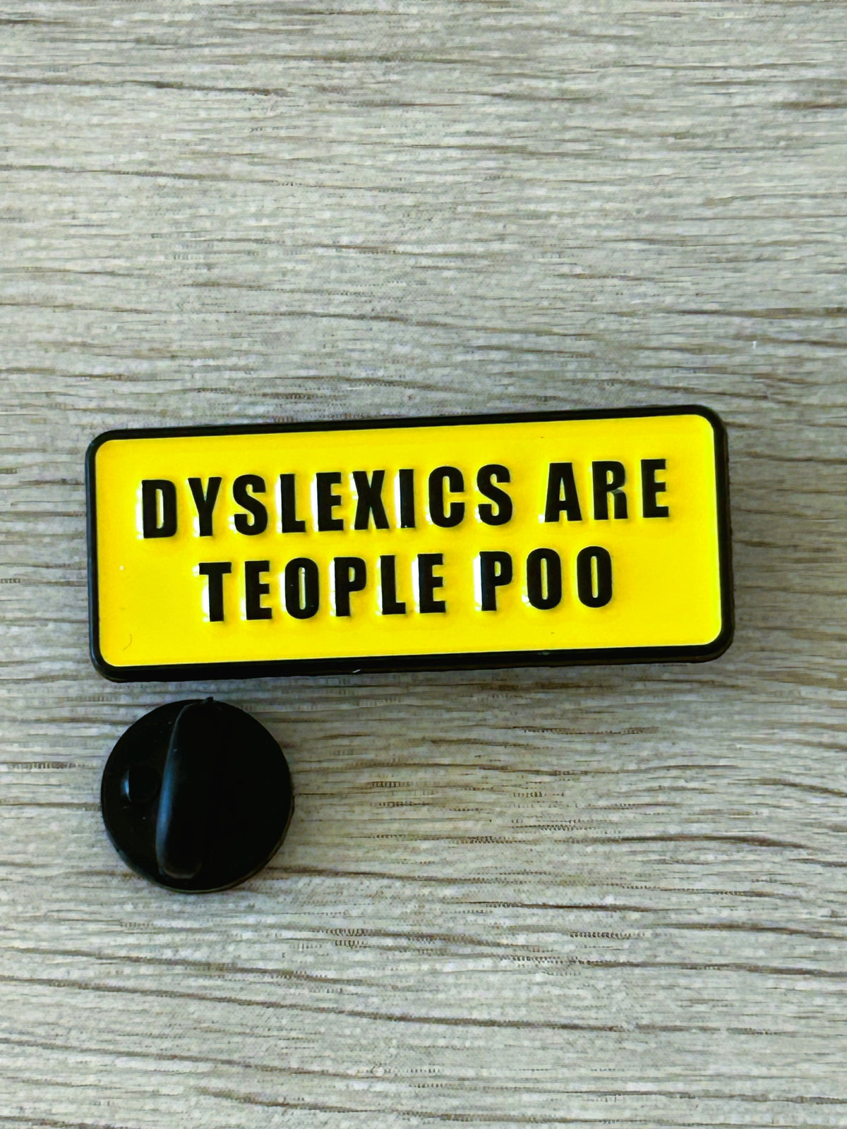 Épingle à badge rectangulaire jaune, texte noir « DYSLEXICS… », avec attache noire