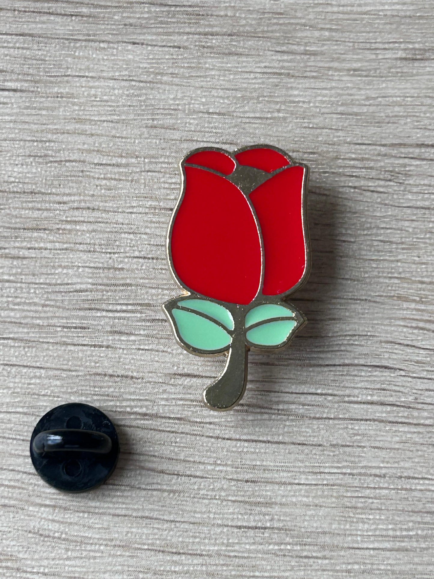 Broche tulipe rouge émaillée avec feuilles vert menthe et attache noire, posée sur fond clair.