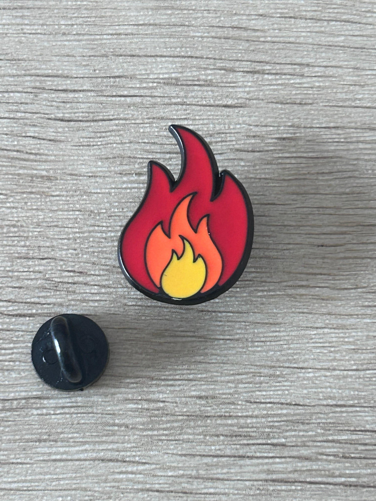 Pin's en forme de flamme rouge et jaune, contour noir, avec fixation