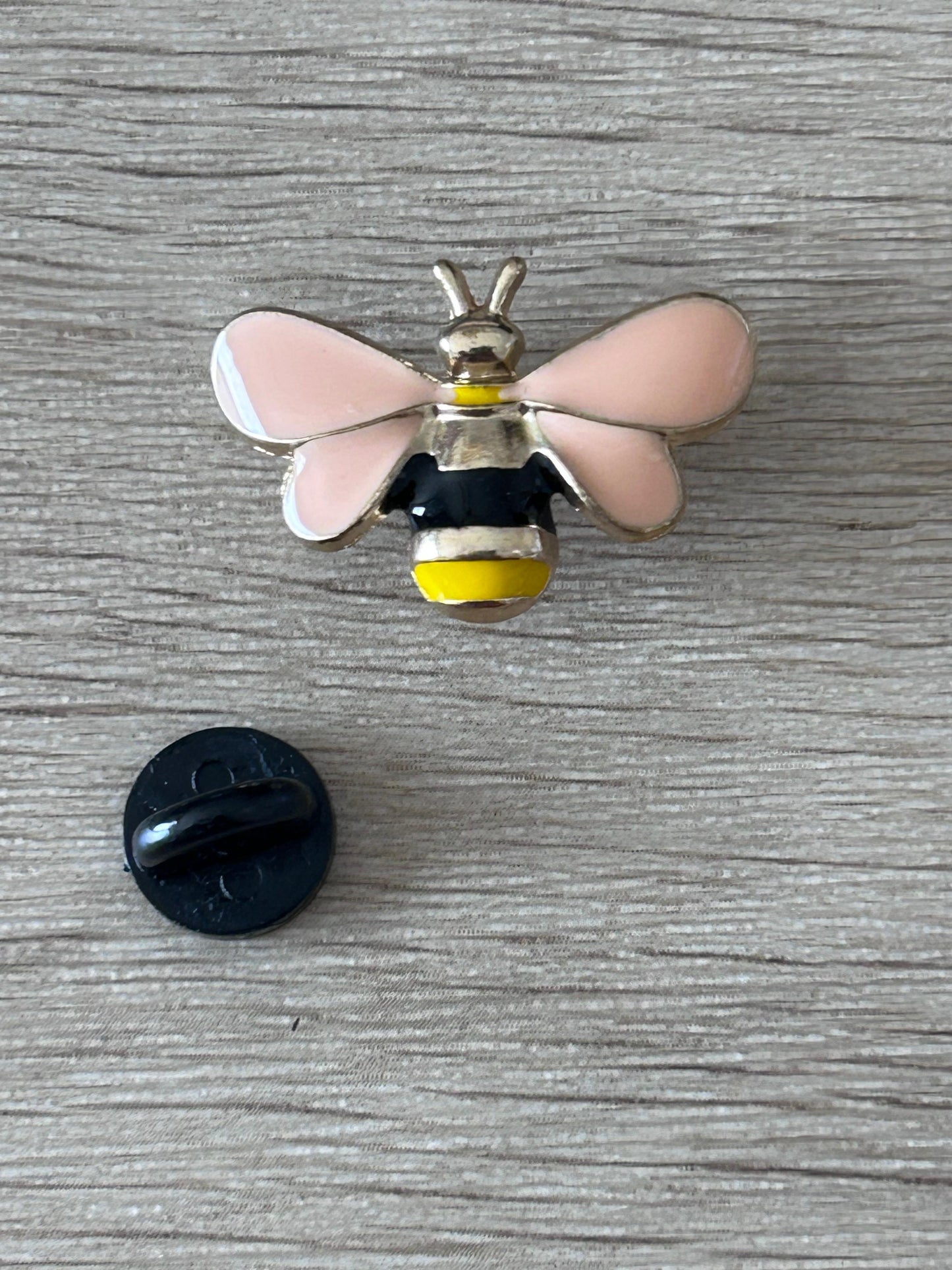 Pin's abeille en relief: ailes roses, corps noir et jaune, avec attache arrière noire.