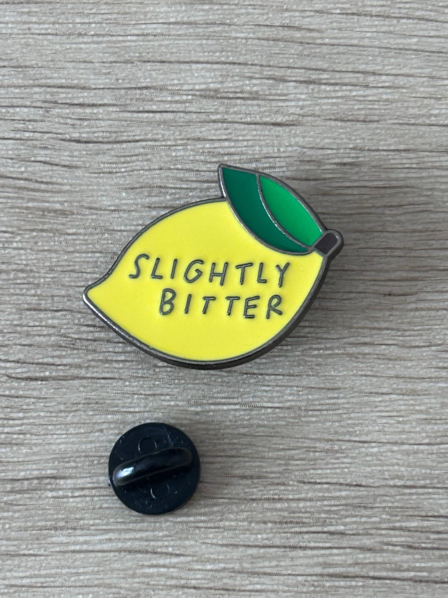 Épingle citron jaune « Slightly Bitter » et feuille verte, dos noir visible.