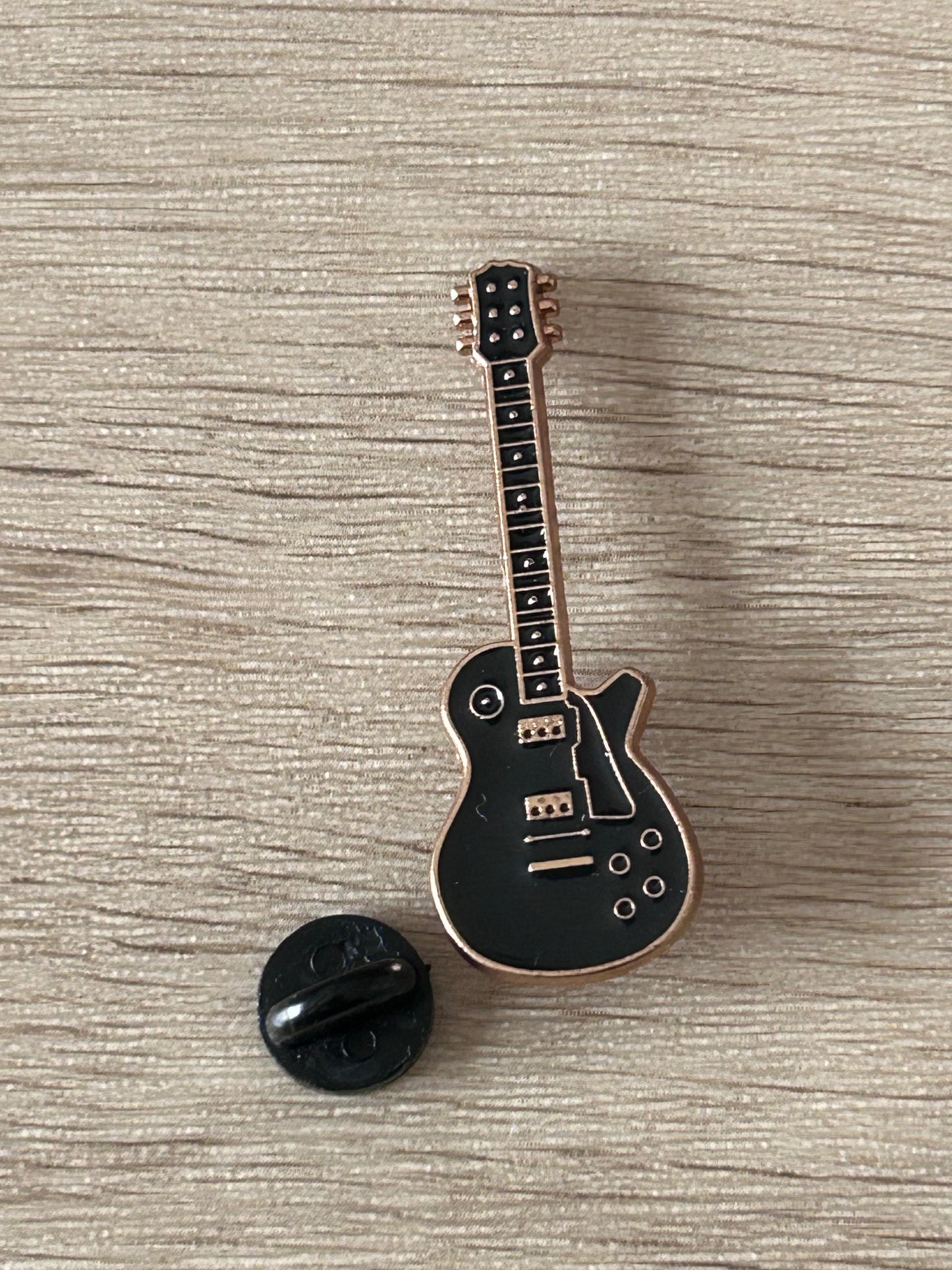Broche guitare électrique noire avec fermeture noire, cordes et boutons visibles.