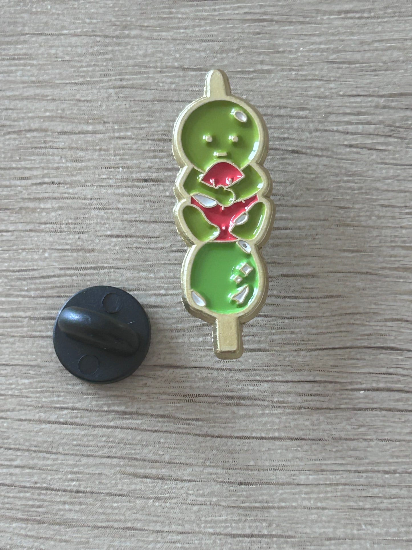 Pin émaillé vert en forme de personnage kawaii, détails rouges en forme de fraise