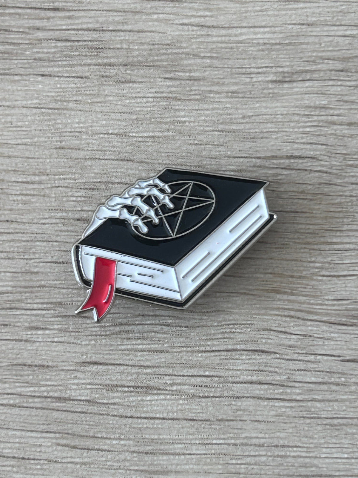 Pin's grimoire noir avec pentagramme, main squelettique et ruban rouge