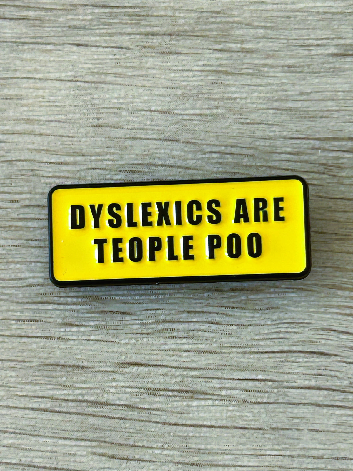 Épingle à badge rectangulaire jaune, texte noir « DYSLEXICS ARE TEOP… »