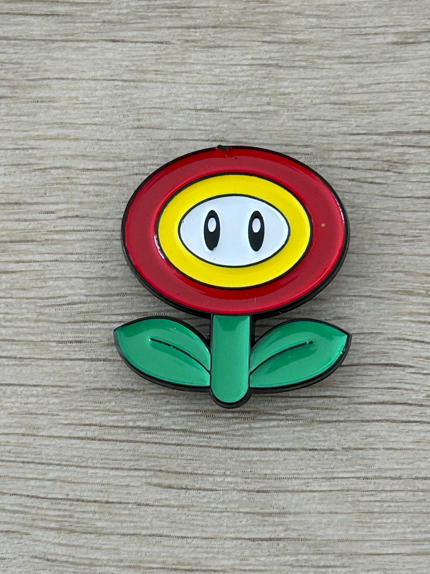 Épinglette fleur de feu Super Mario, face jaune dans anneau rouge, feuilles vertes