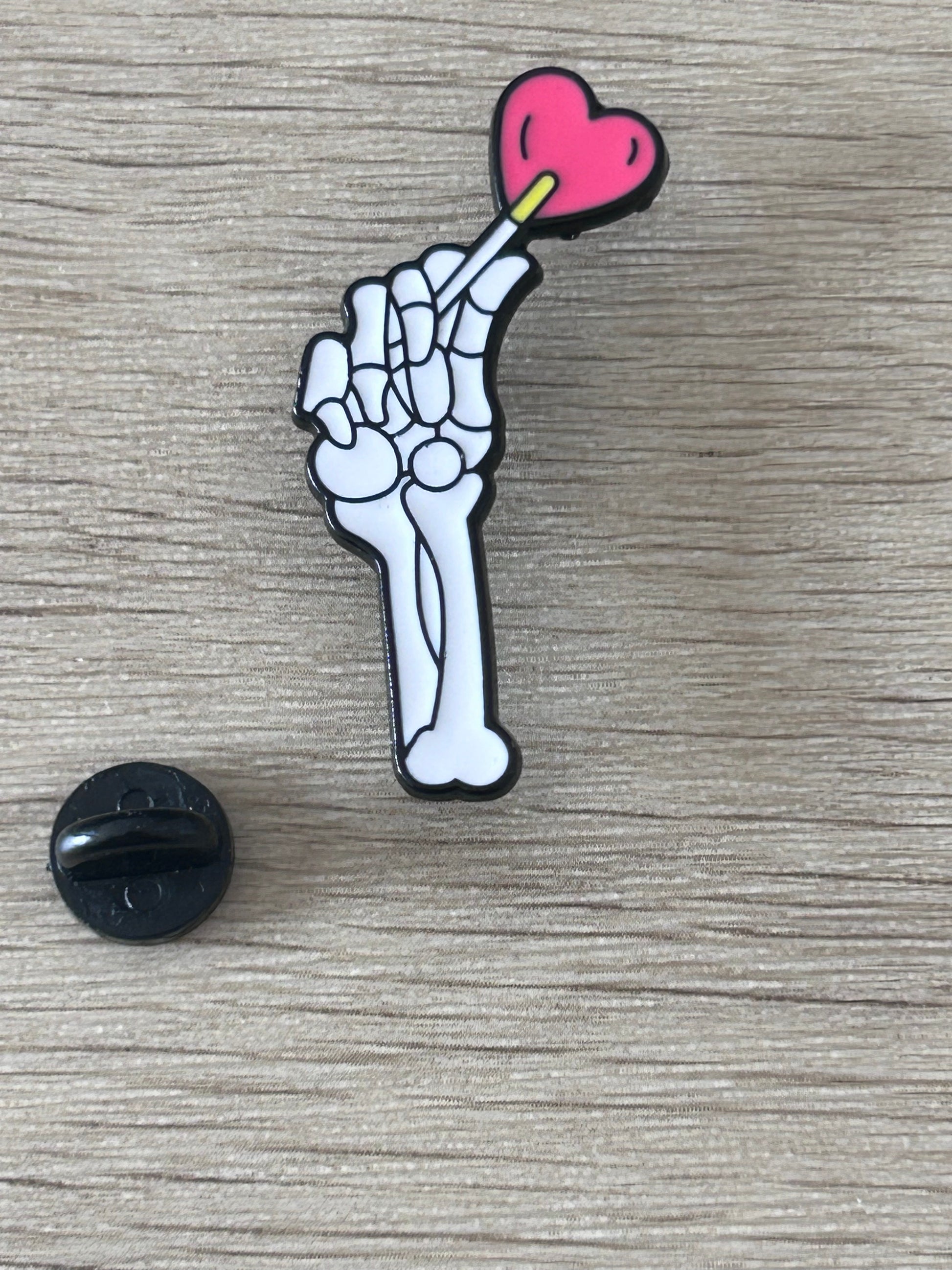 Épinglette en forme de main de squelette tenant un cœur rose