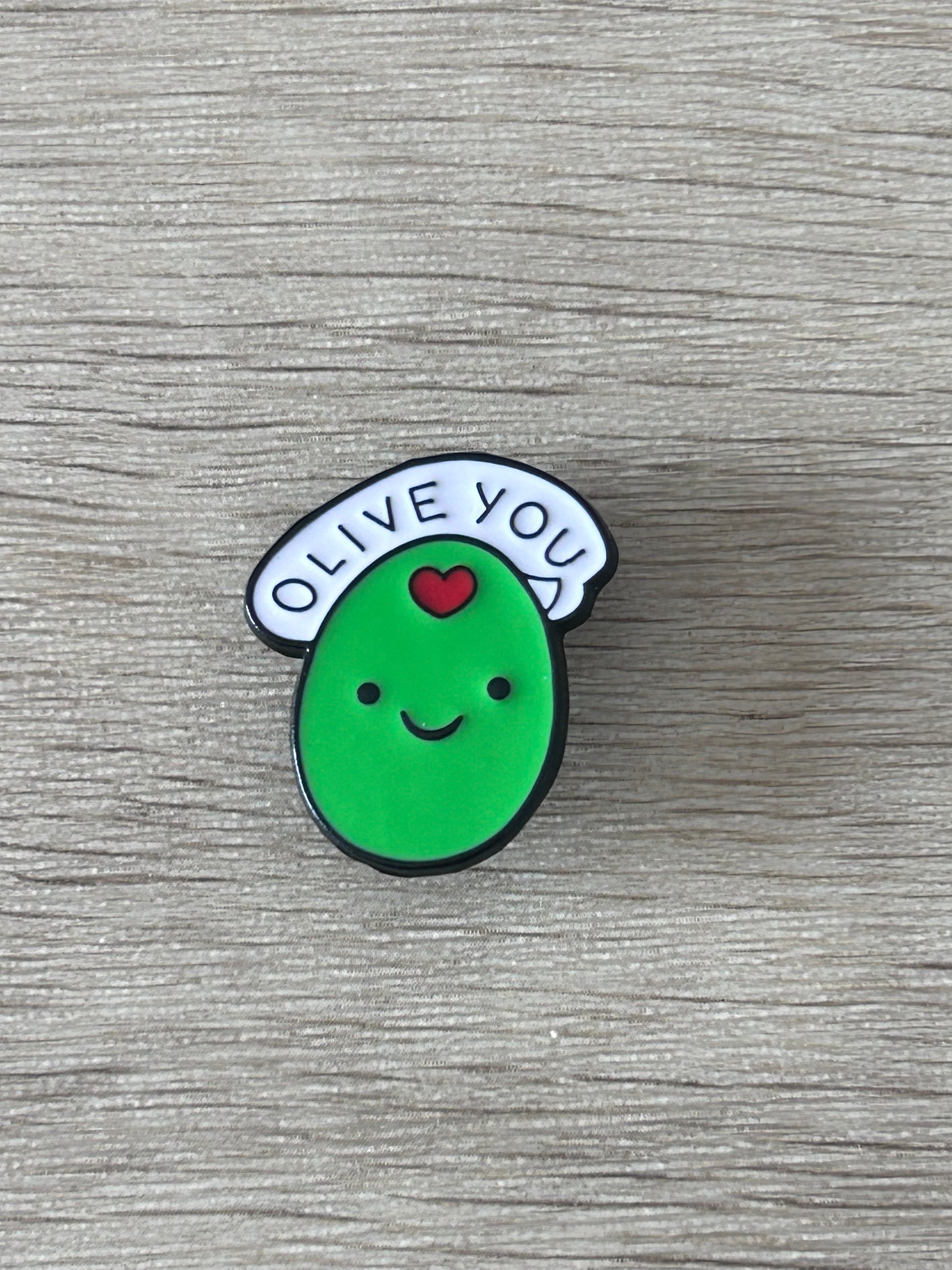 Épingle en forme d’olive verte « OLIVE YOU » avec visage souriant et cœur rouge.