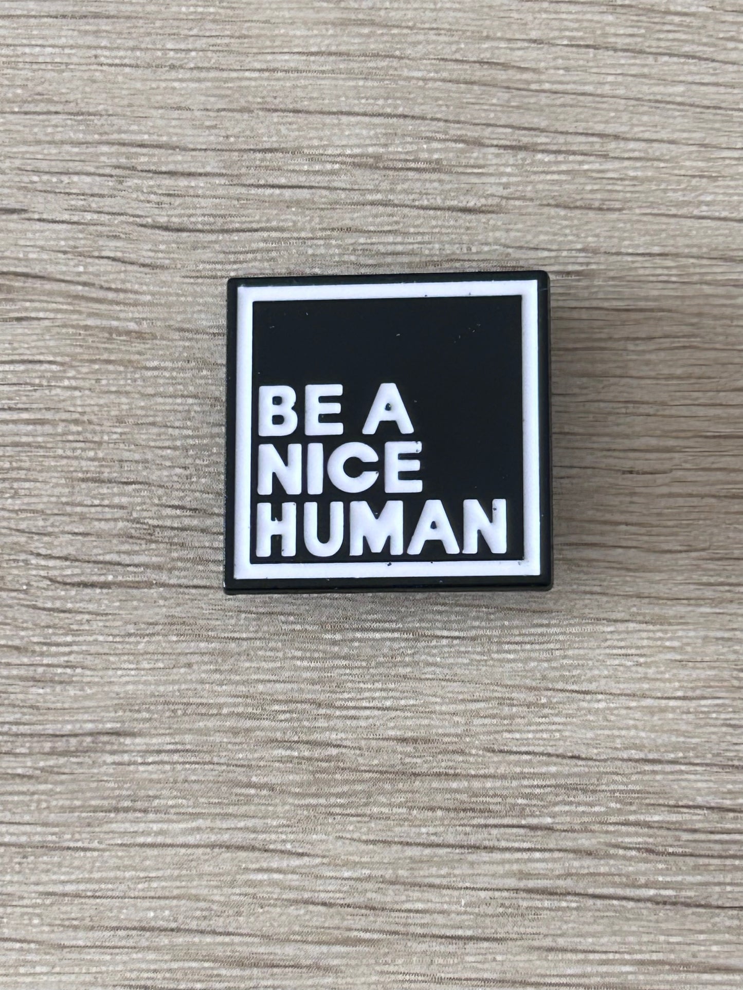 Pin carré noir et blanc « BE A NICE HUMAN » avec bordure argentée