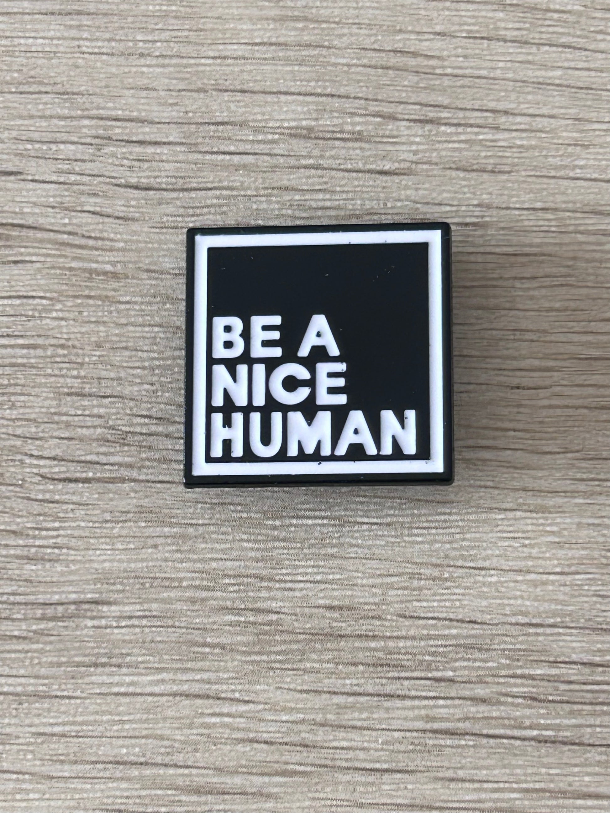 Pin carré noir et blanc « BE A NICE HUMAN » avec bordure argentée