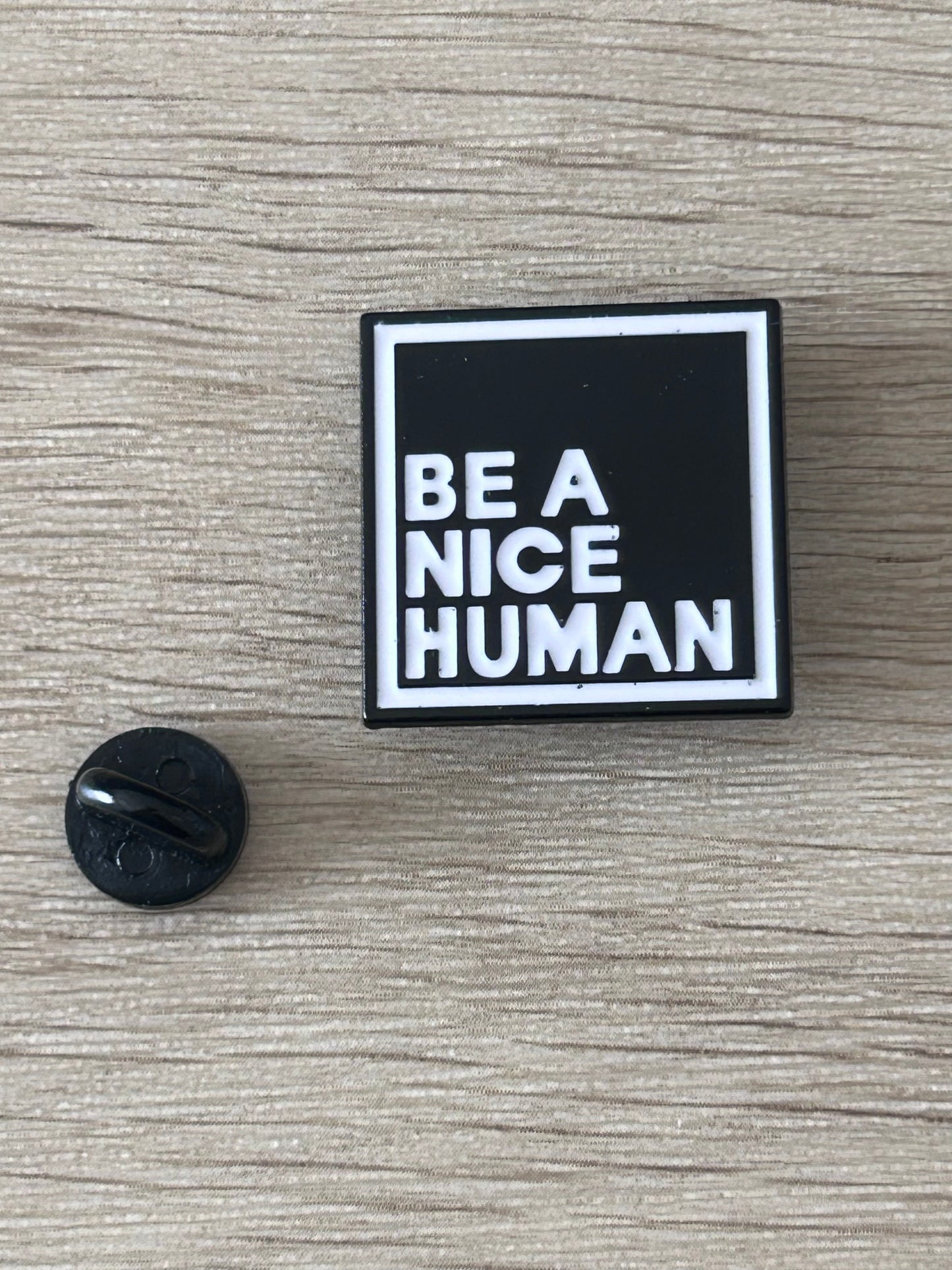 Pin carré « BE A NICE HUMAN » noir et blanc, et dos noir du fermoir