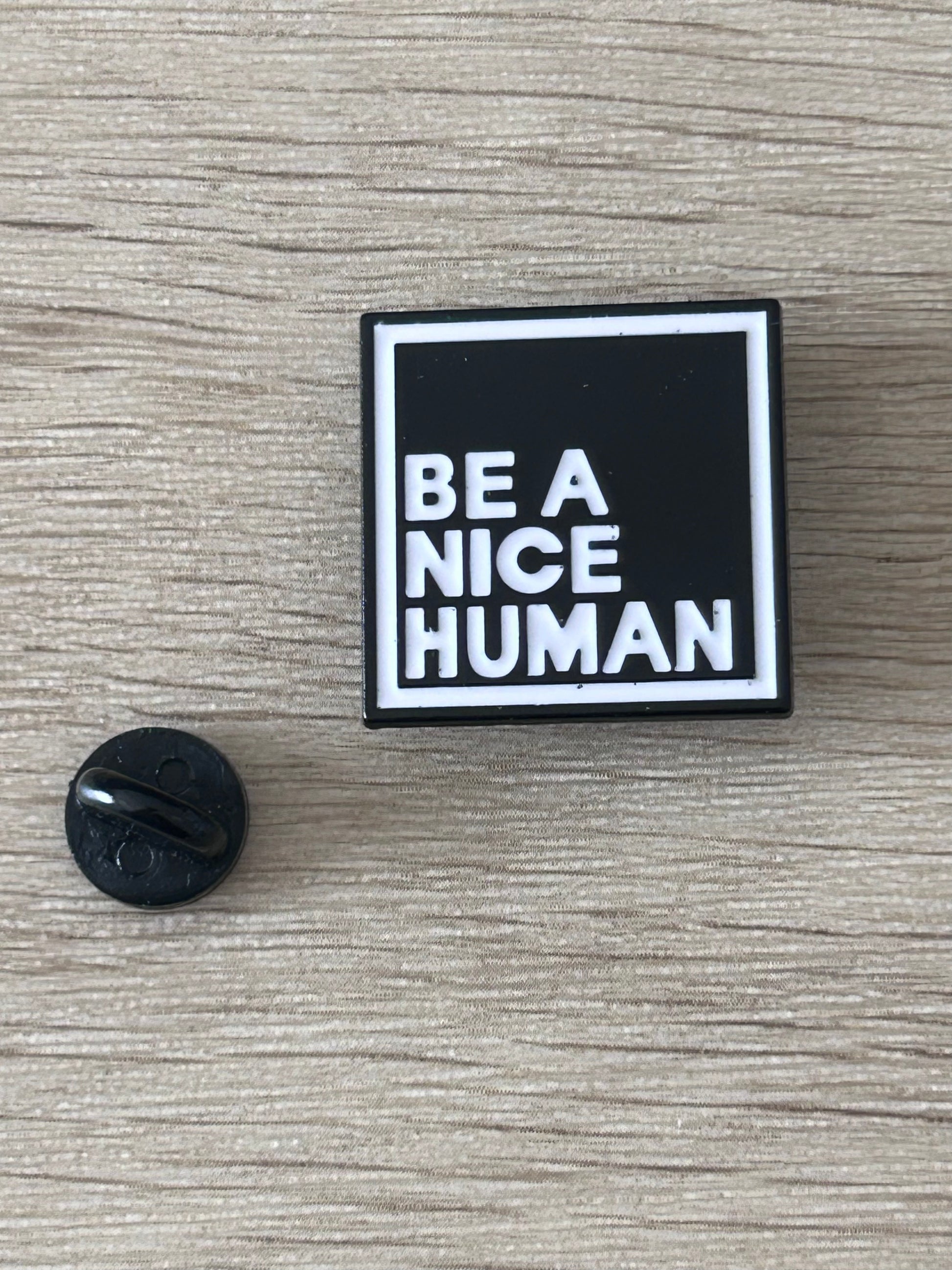 Pin carré « BE A NICE HUMAN » noir et blanc, et dos noir du fermoir