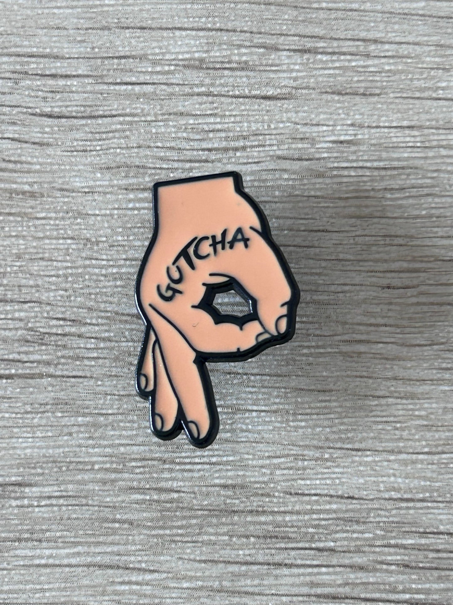 Épinglette en forme de main rose, « GOTCHA » sur le poing noir