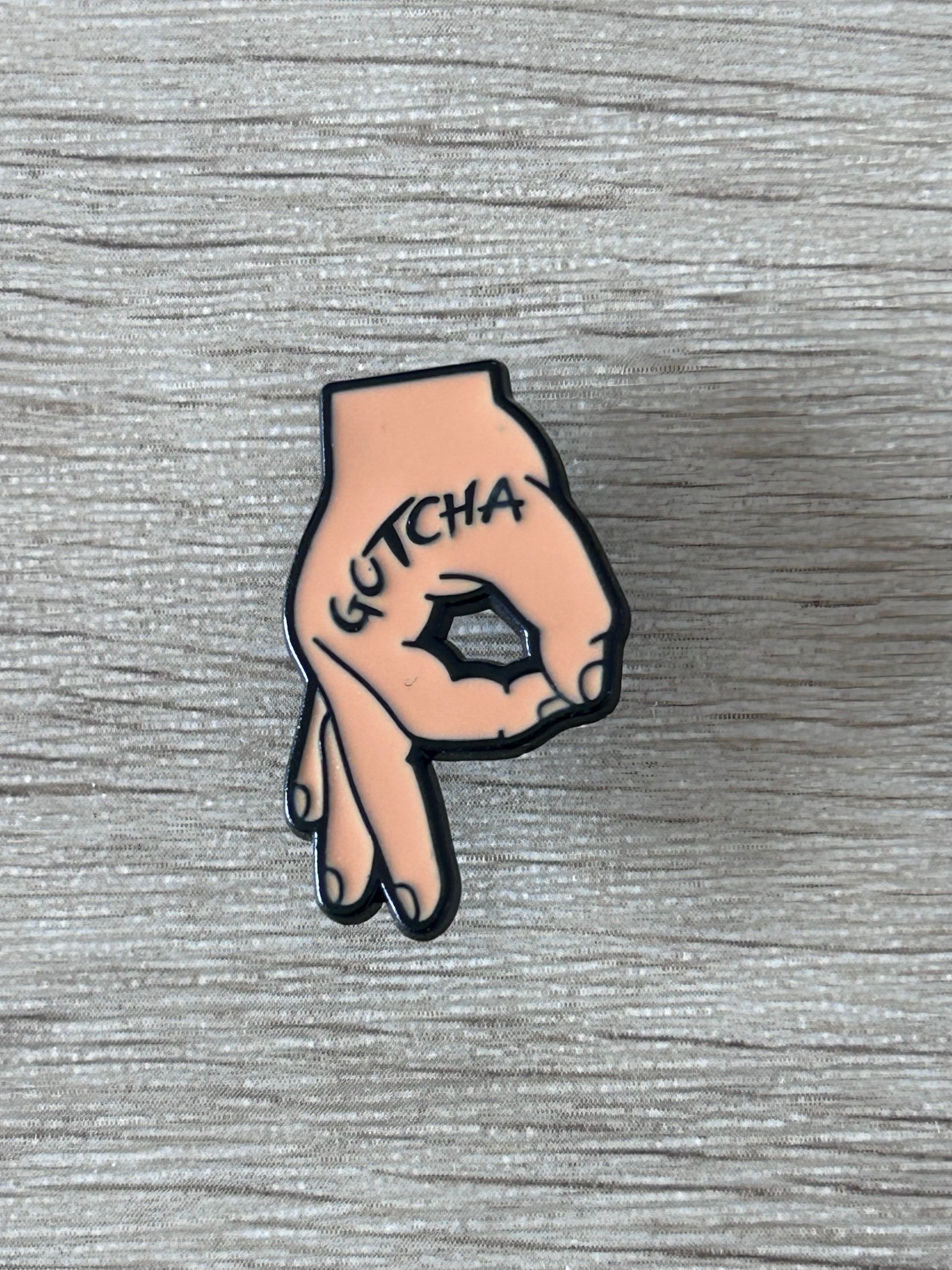 Épinglette en forme de main rose, « GOTCHA » sur le poing noir