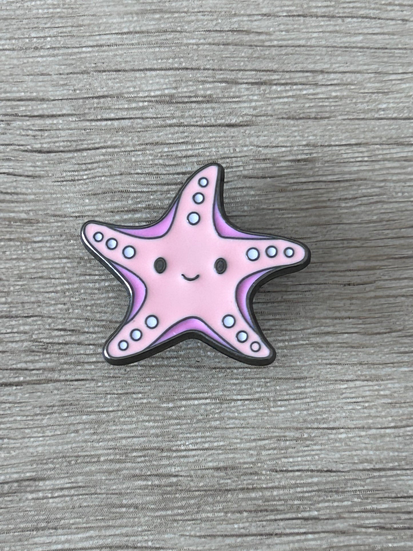 Pin's en forme d’étoile de mer kawaii rose, sourire et points bleus, contour noir.