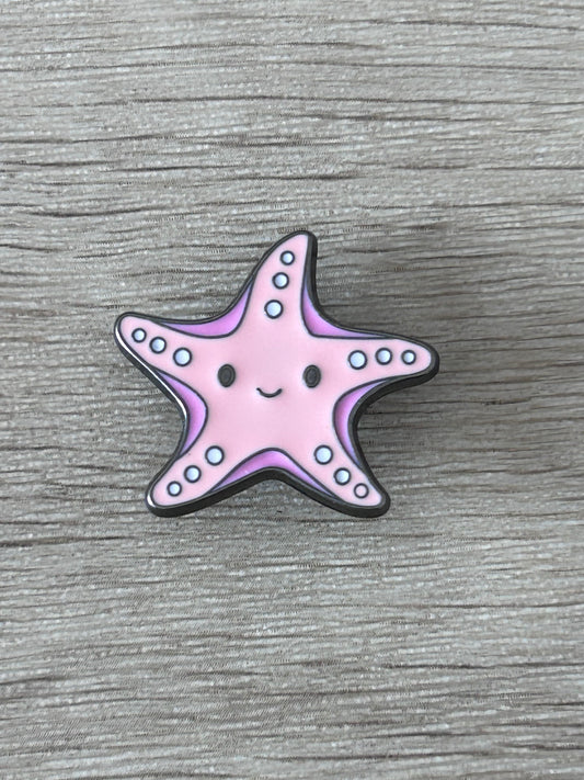Pin's en forme d’étoile de mer kawaii rose, sourire et points bleus, contour noir.