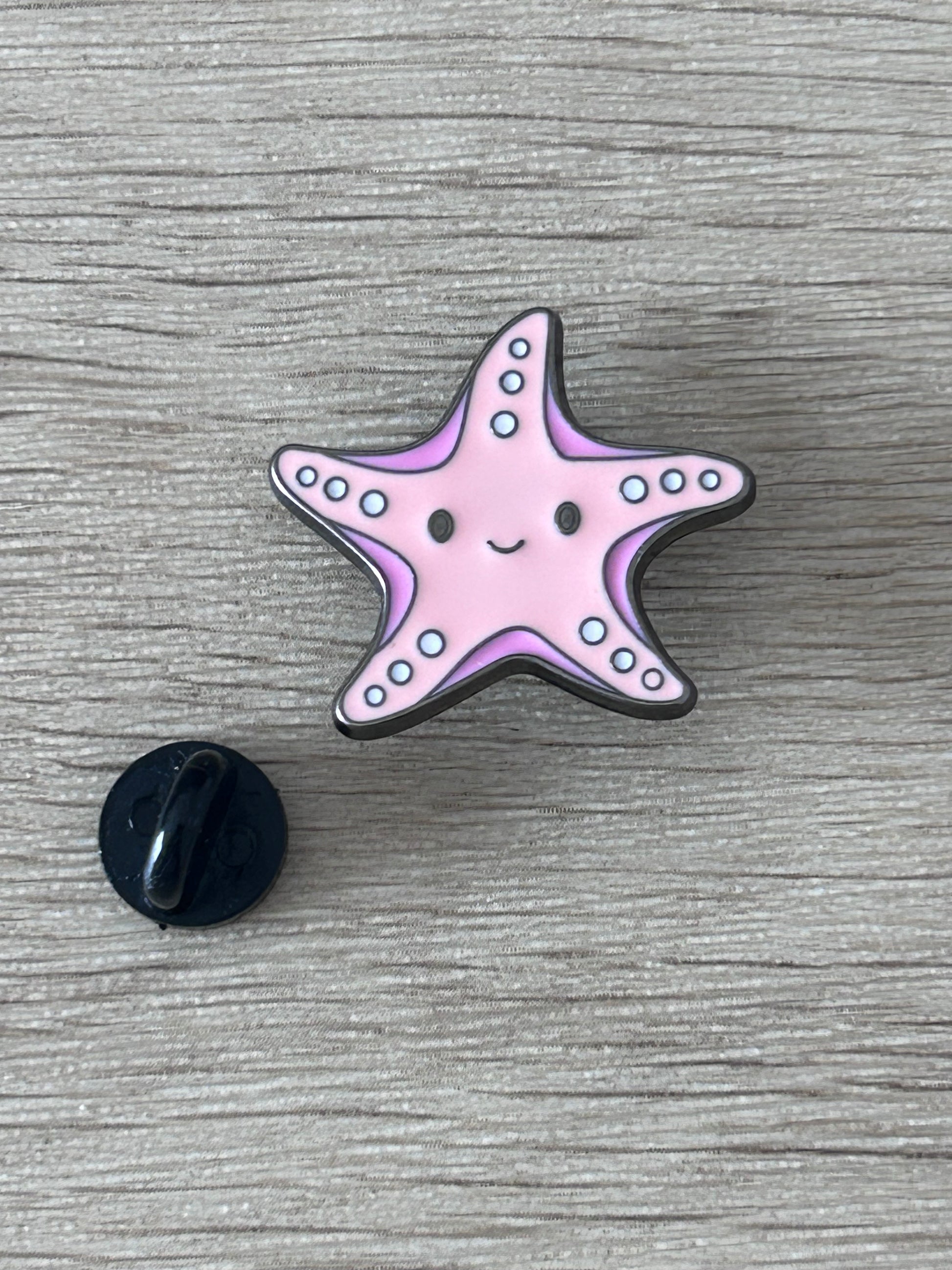 Pin's en forme d’étoile de mer kawaii rose avec dos noir rond, points bleus.