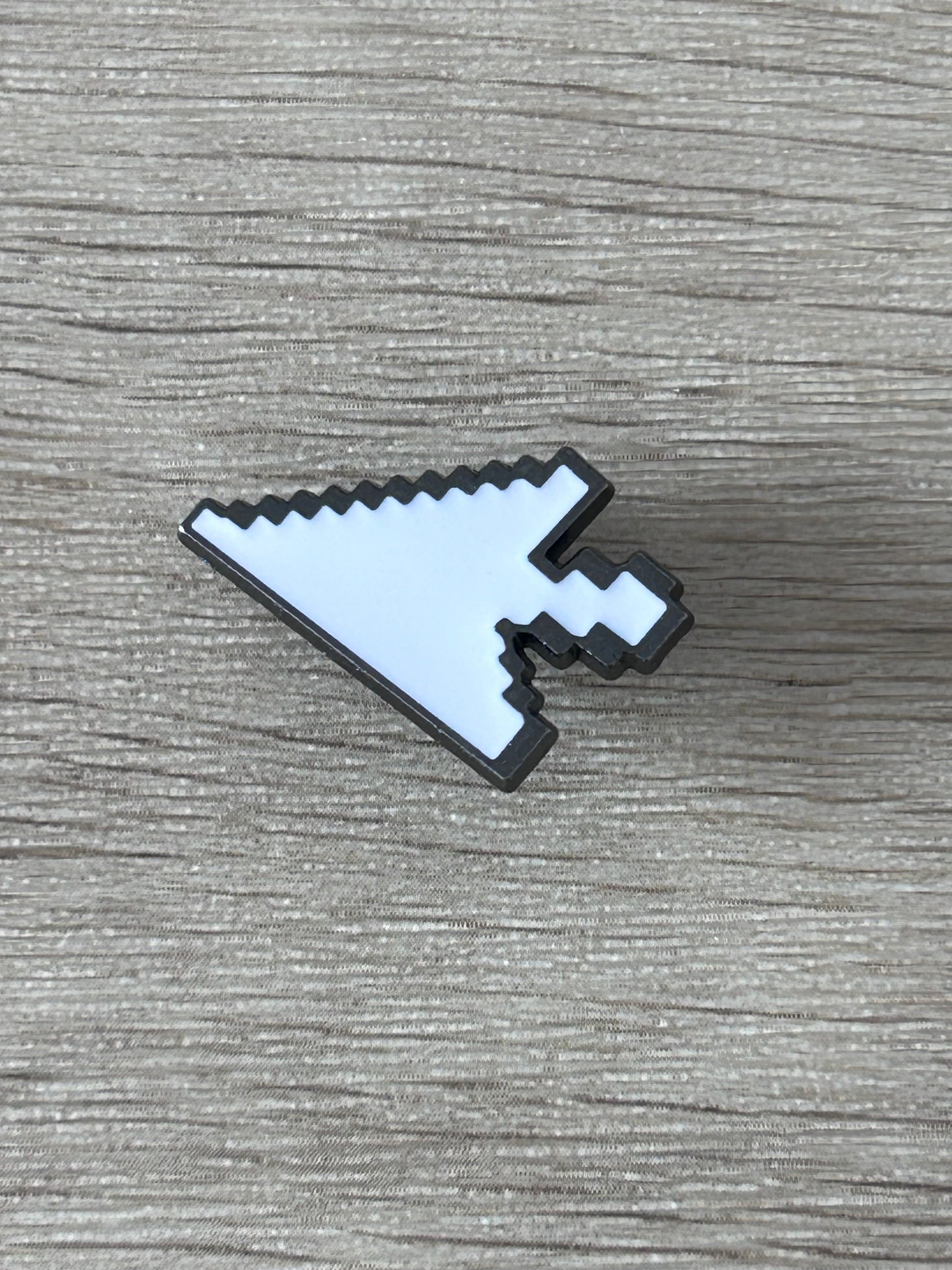 Épingle curseur pixel blanche bleutée avec bord et détails noirs, posée à plat.