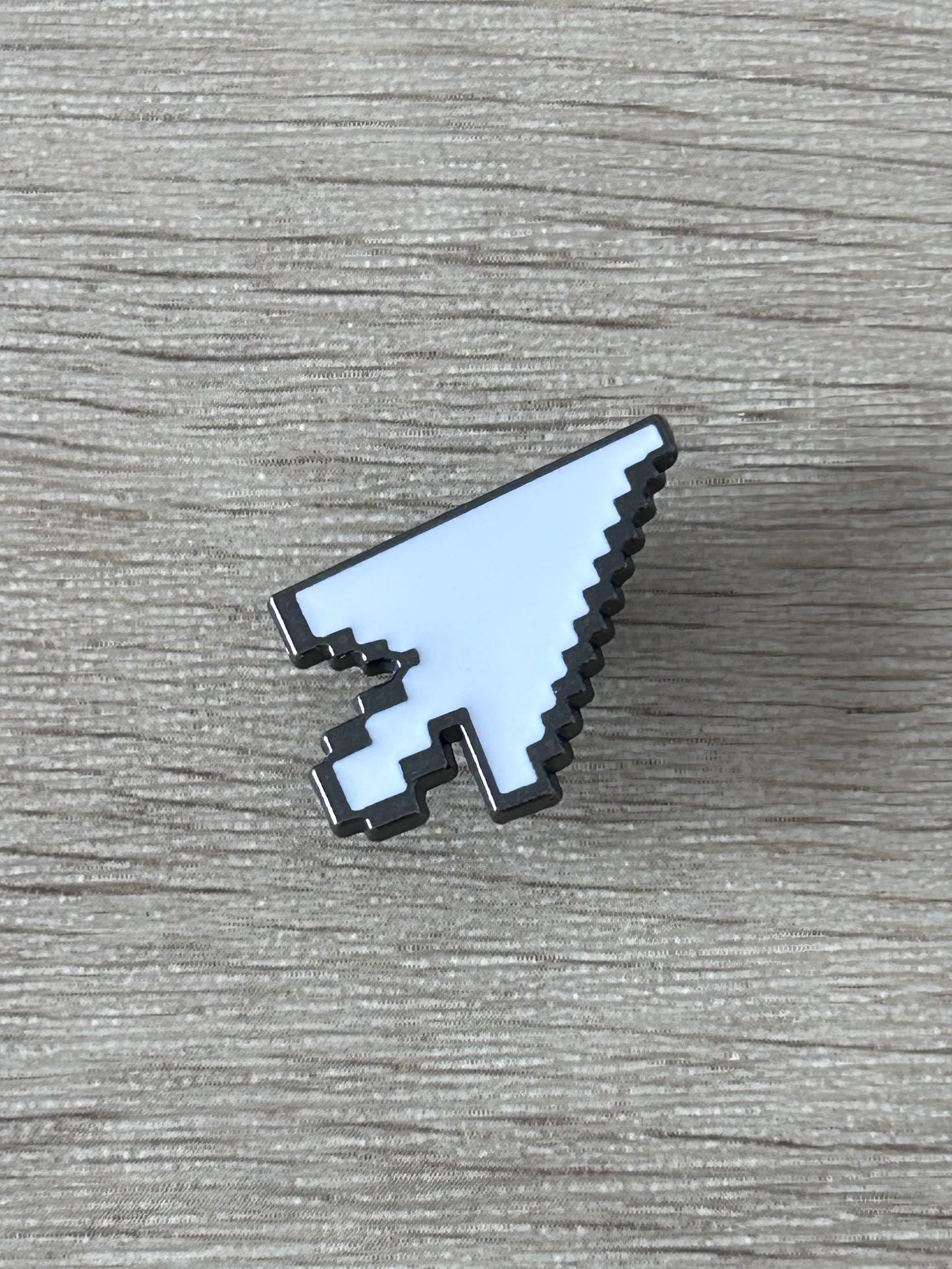 Épingle en forme de curseur pixel, plaque blanche bleutée et détails noirs, vue de côté.