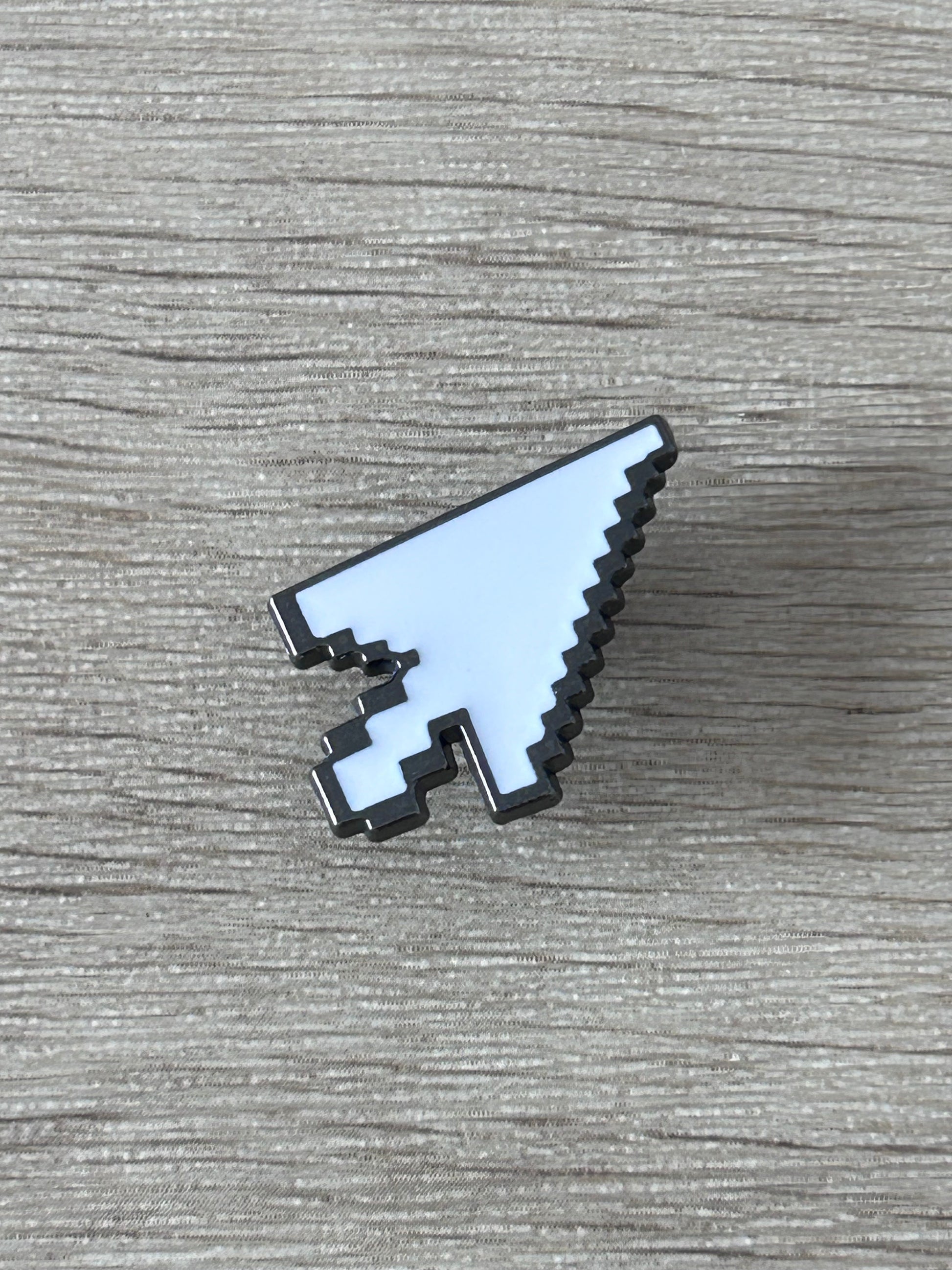 Épingle en forme de curseur pixel, plaque blanche bleutée et détails noirs, vue de côté.