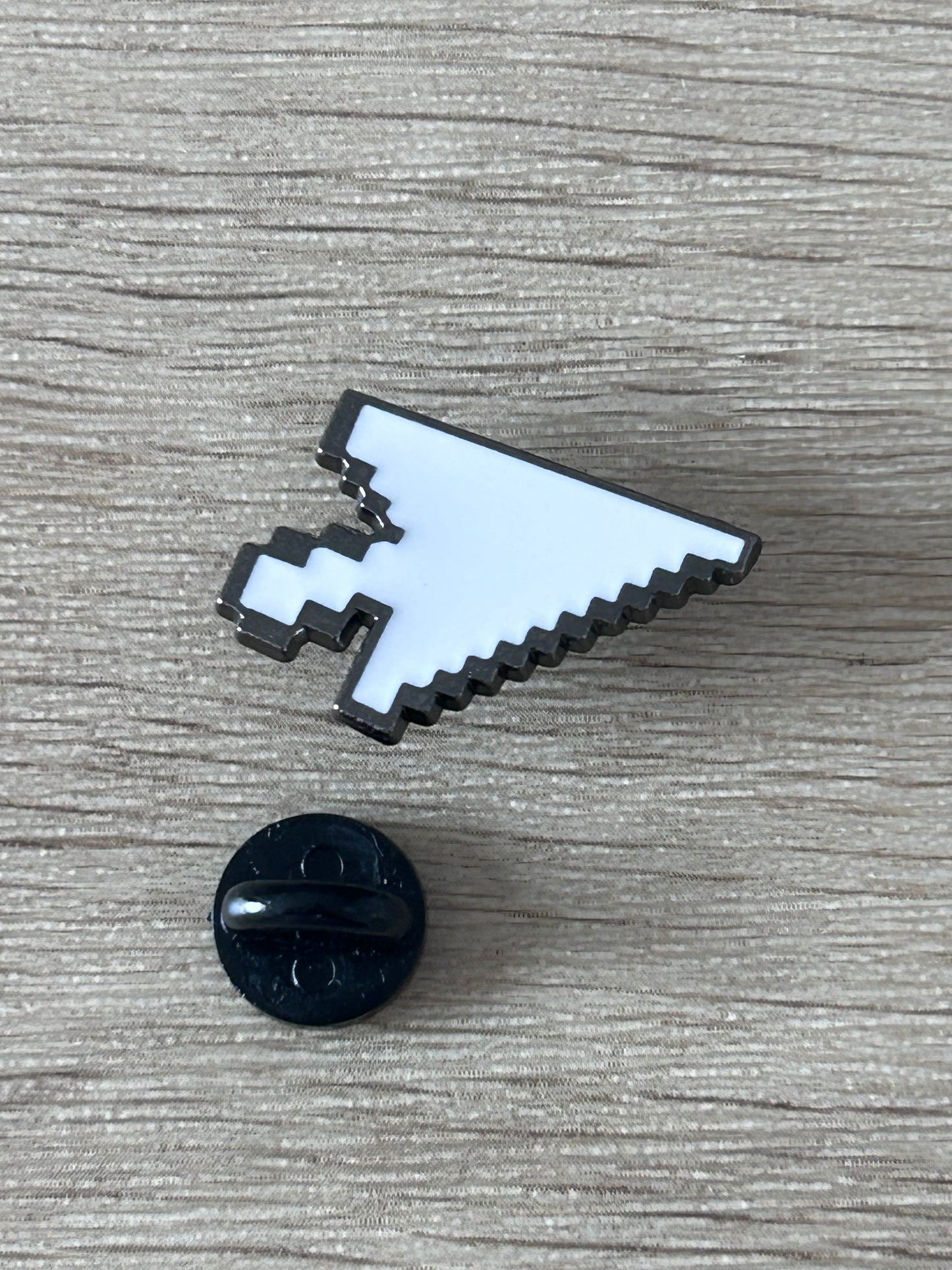 Épingle émaillée en forme de curseur pixel, blanc bleu et noir; avec petit élément rond noir.