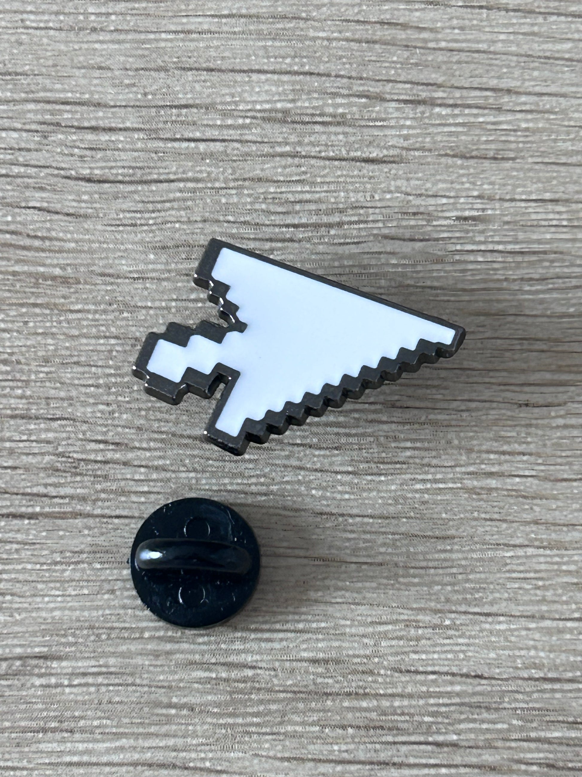 Épingle émaillée en forme de curseur pixel, blanc bleu et noir; avec petit élément rond noir.