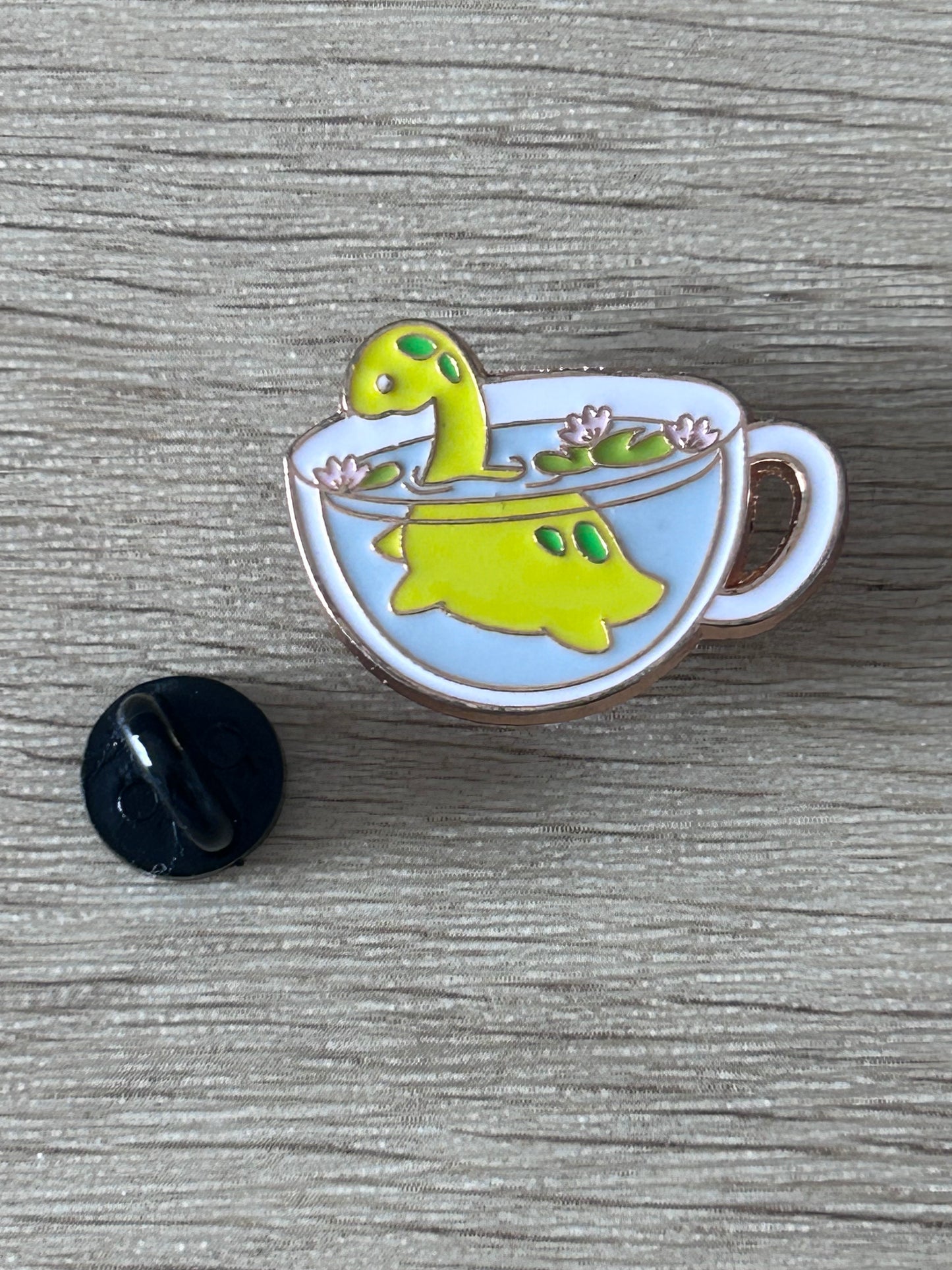 Épingle émail Nessie dans une tasse de thé bleu clair, vue de face, fleurs roses