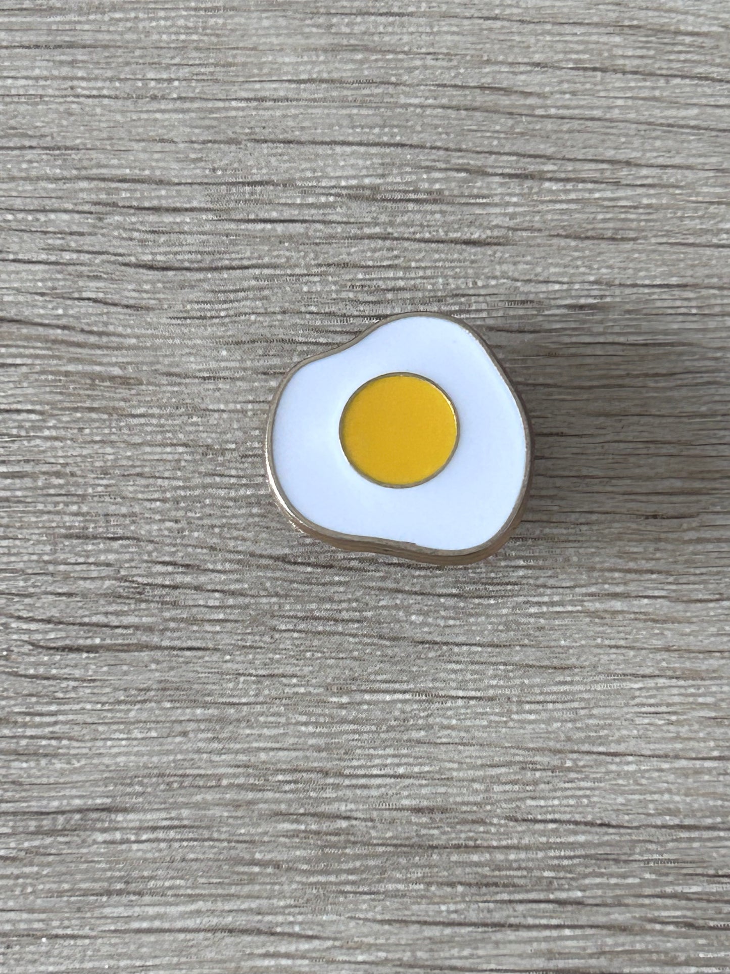 Épingle en forme d’œuf au plat, émail blanc et jaune, contour argent.