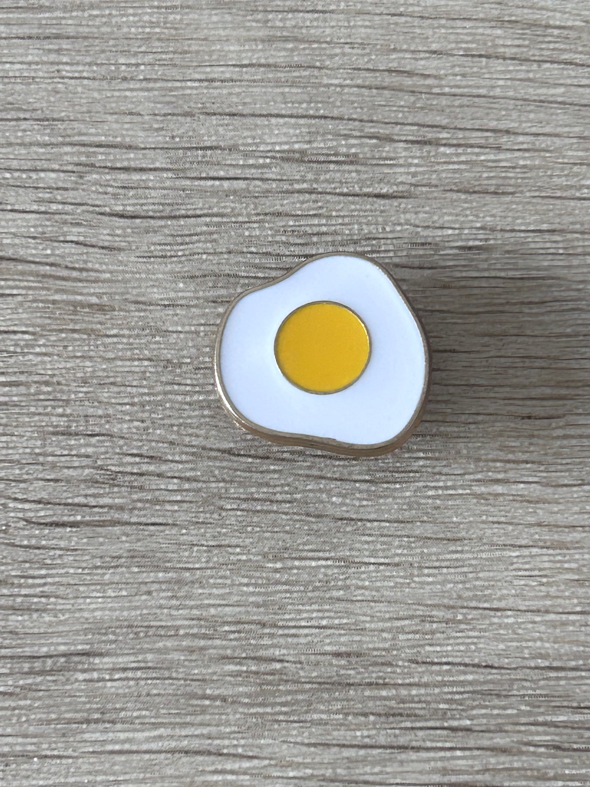 Épingle en forme d’œuf au plat, émail blanc et jaune, contour argent.