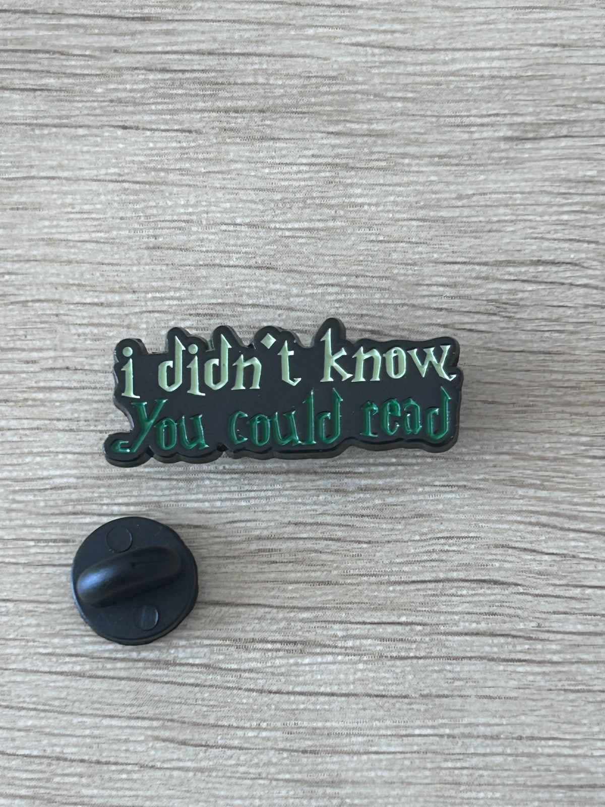 Pin émaillé vert foncé/noir avec inscription, et attache ronde au revers