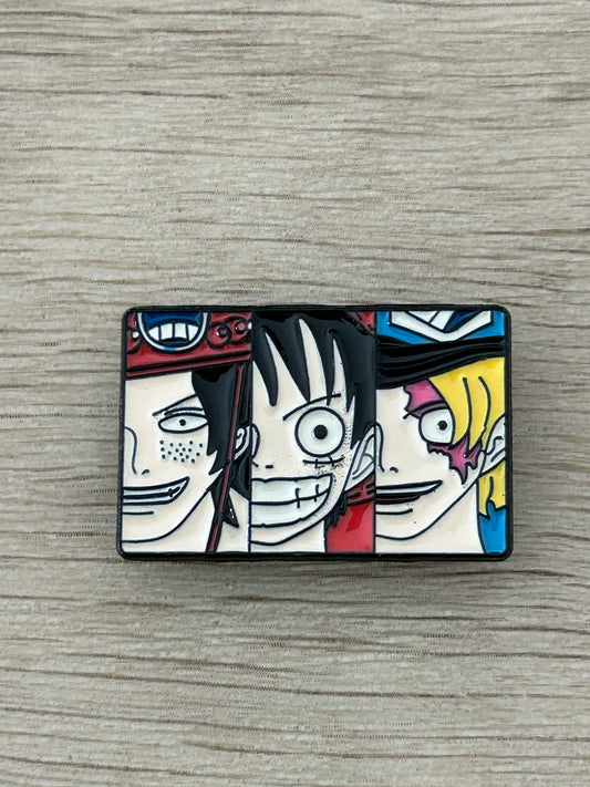Épingle rectangulaire noire avec trois visages d’anime, contours blancs et colorés