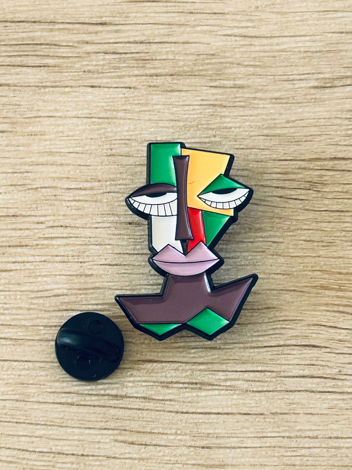 Pin visage cubiste multicolore avec fermoir noir au dos.