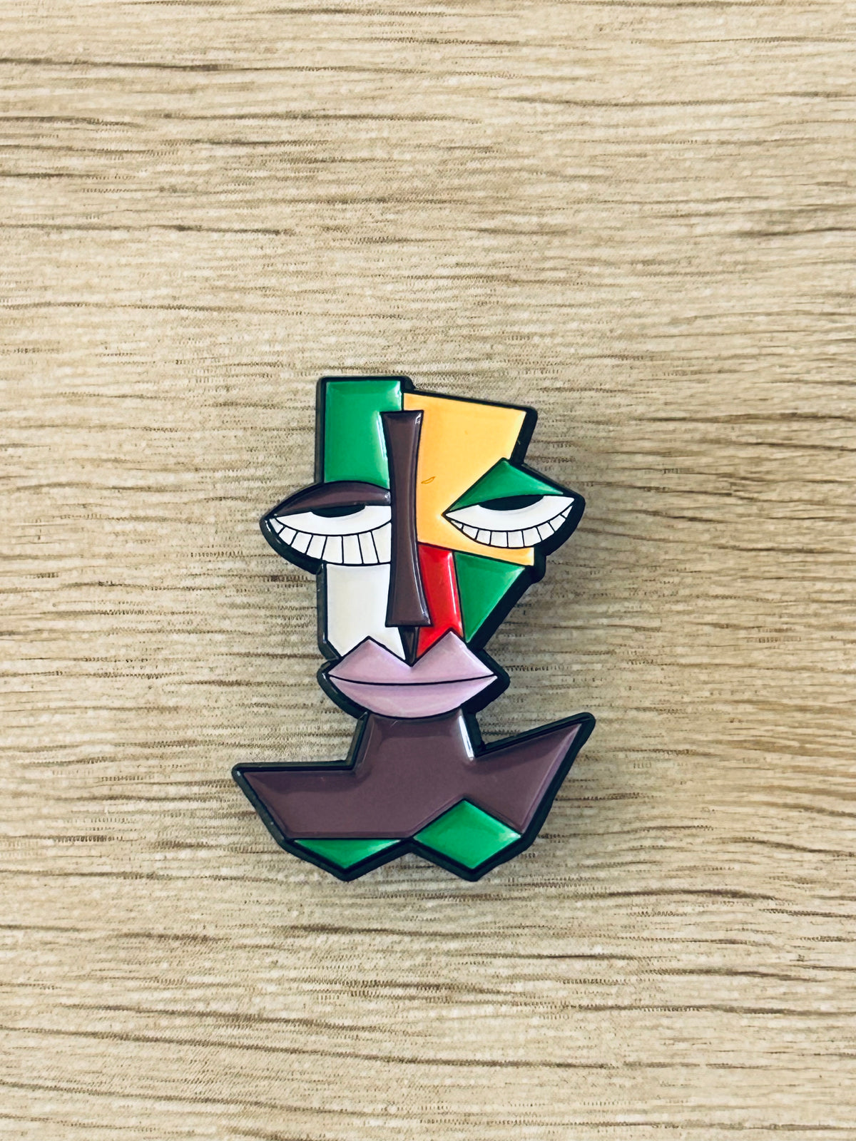 Pin visage cubiste multicolore en forme de face géométrique, yeux blancs et bouche rose.