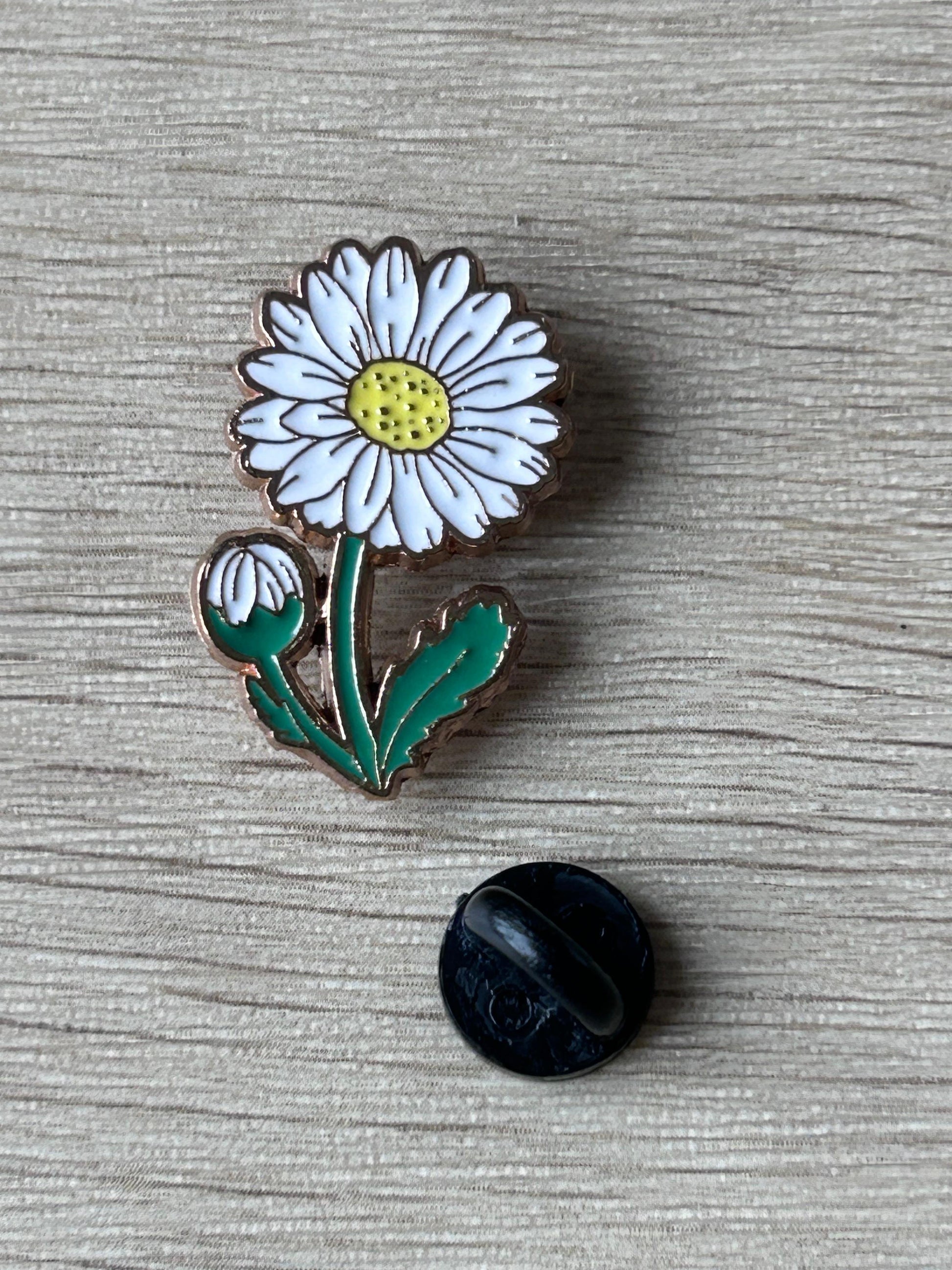 Pin's marguerite émaillé avec dos noir rond; fleur blanche, cœur jaune, feuilles vertes.