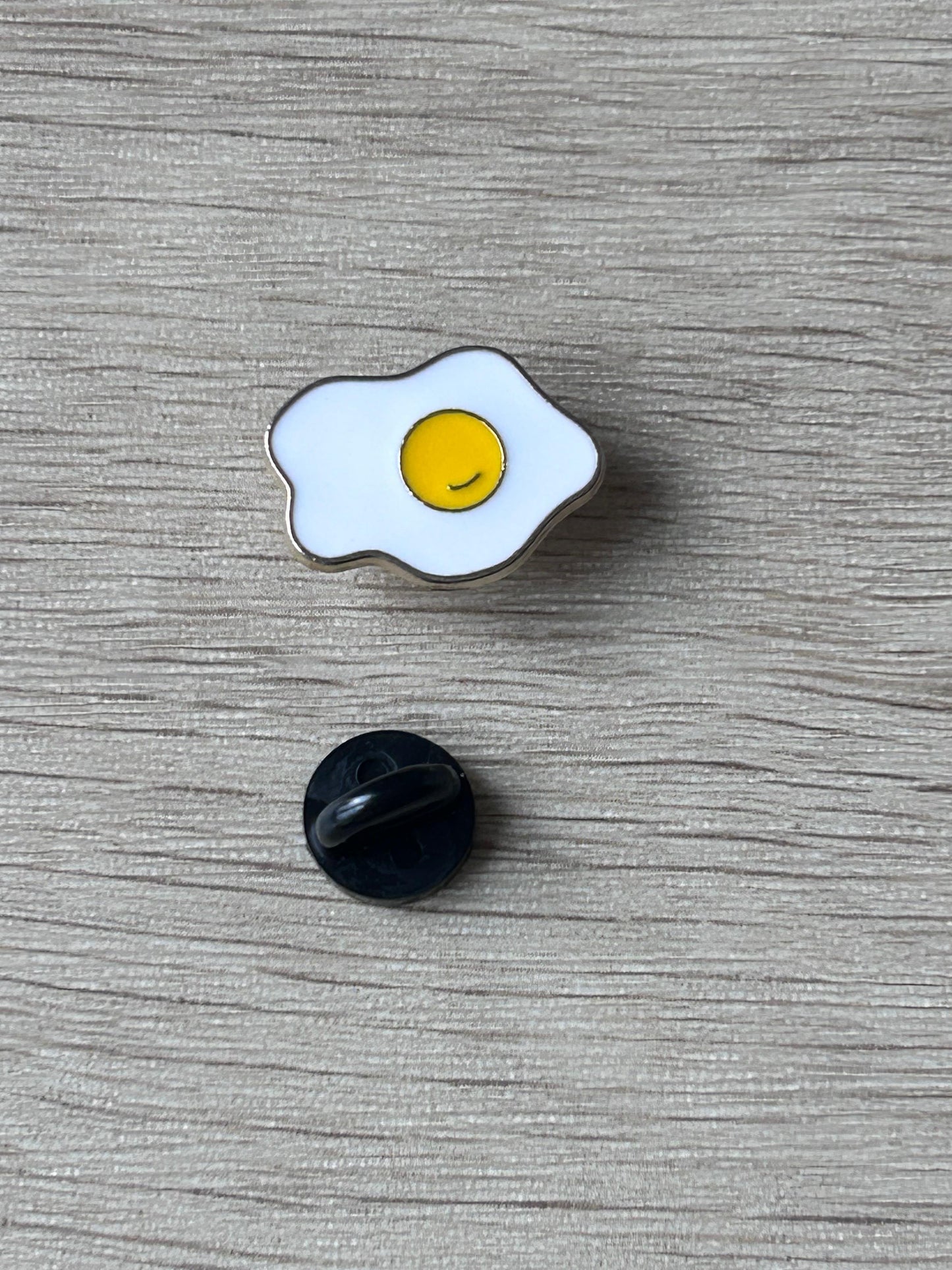 Broche œuf au plat émaillé blanc et jaune avec support arrière noir visible.