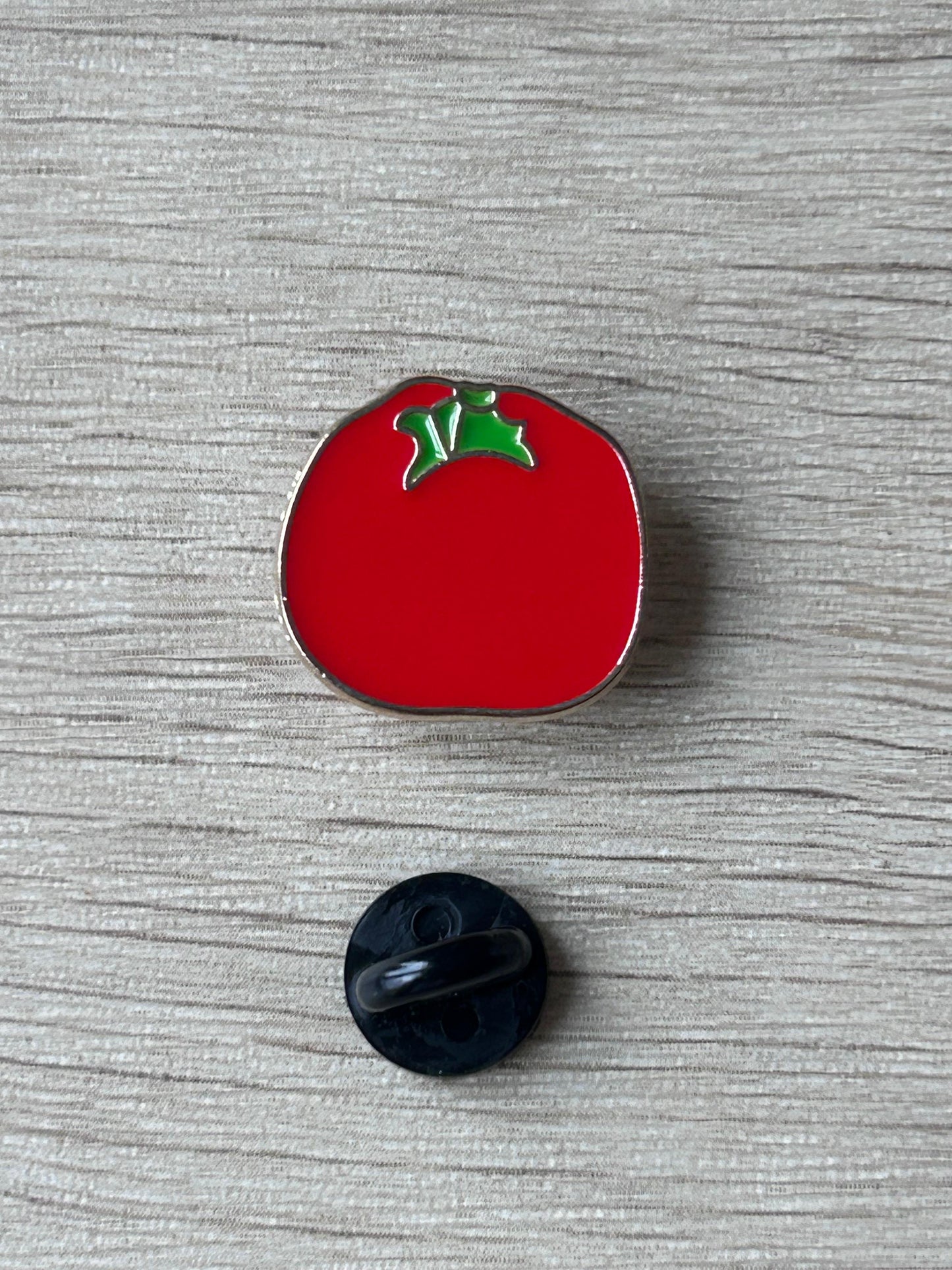 Pin's tomate rouge émaillé, bord argenté, feuilles vertes; dos noir visible