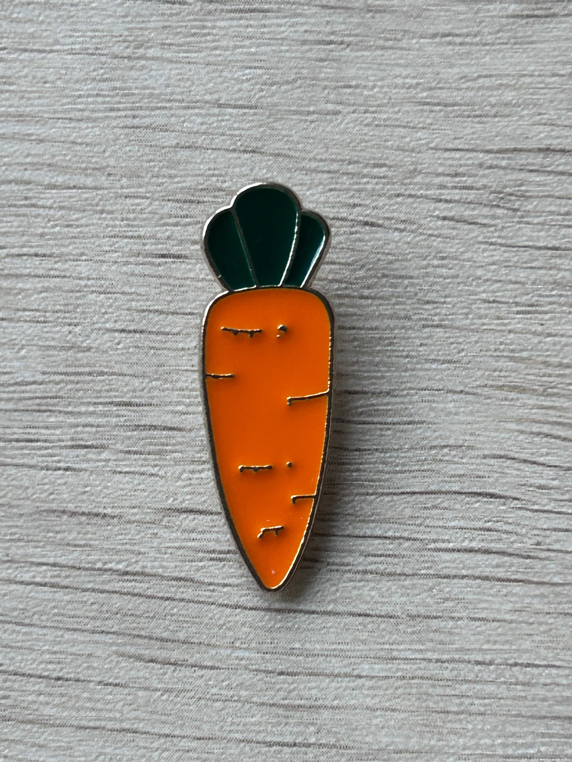 Broche en forme de carotte orange avec tige vert foncé, vue de face.