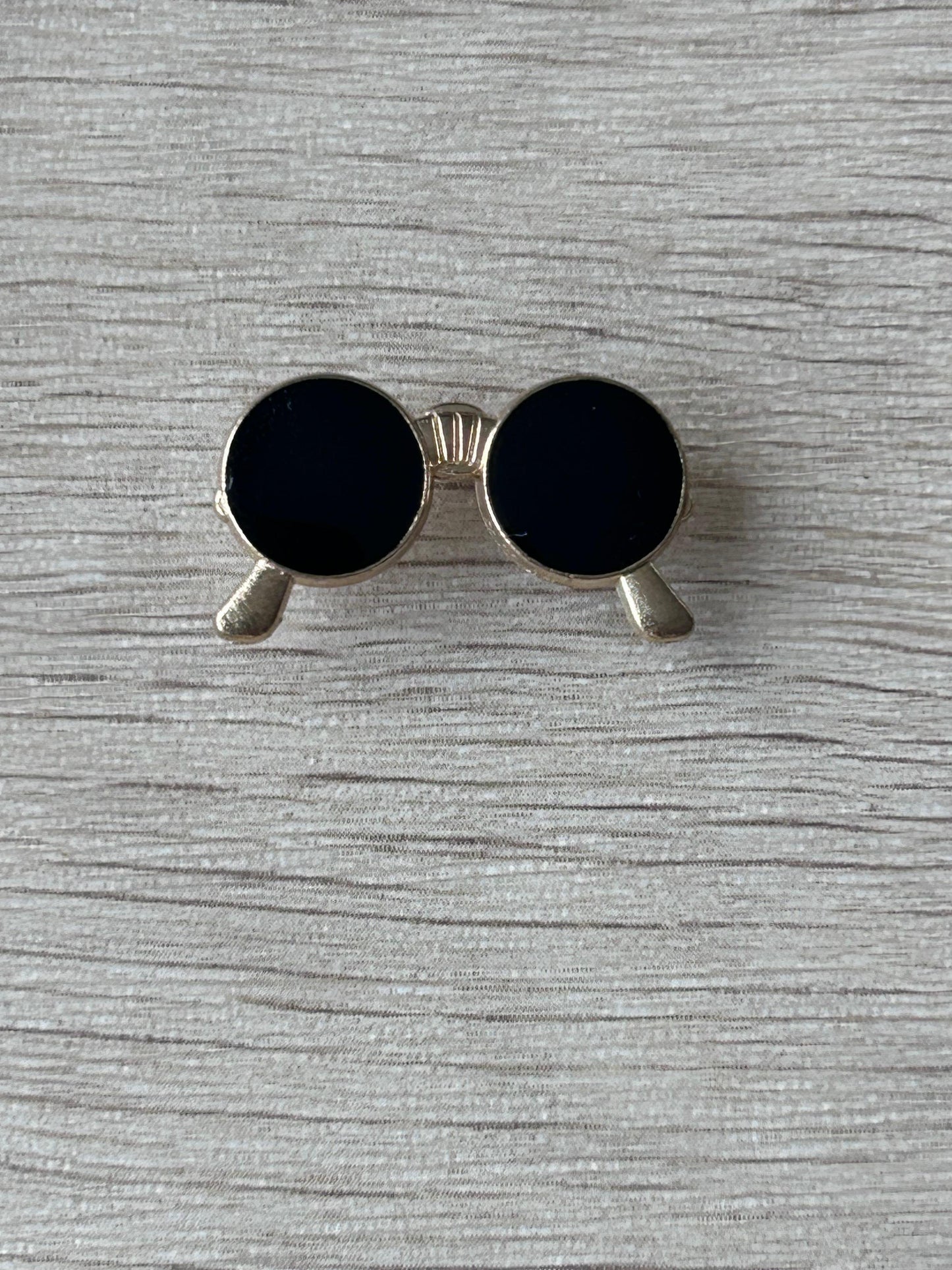 Broche lunettes rondes noires : monture argentée et embouts gris, verres noirs.