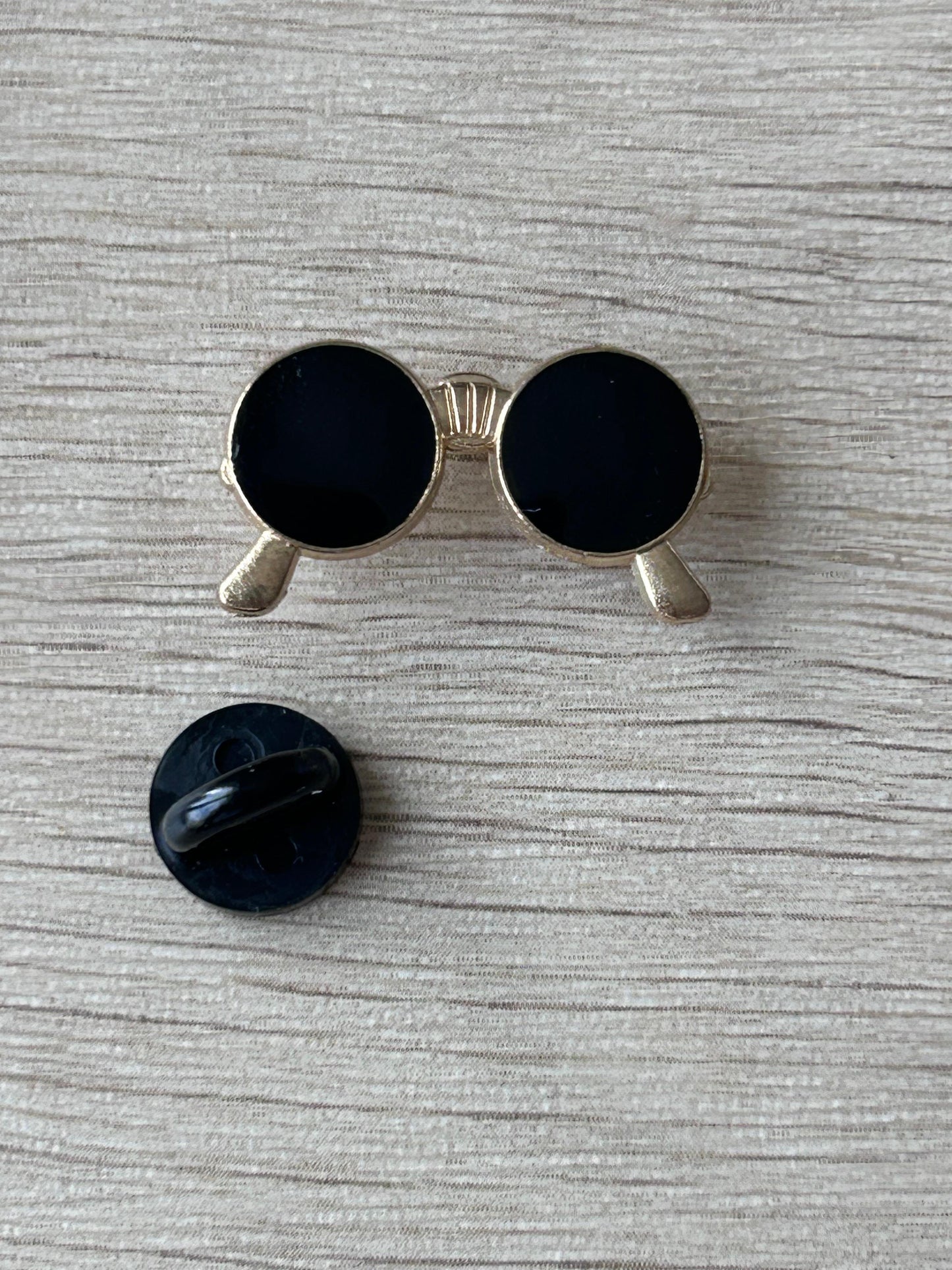 Broche lunettes rondes noires avec dos noir rond, monture argentée et verres foncés.