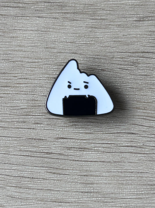 Épingle en forme d’onigiri blanc, visage grognon et contour bleu foncé.
