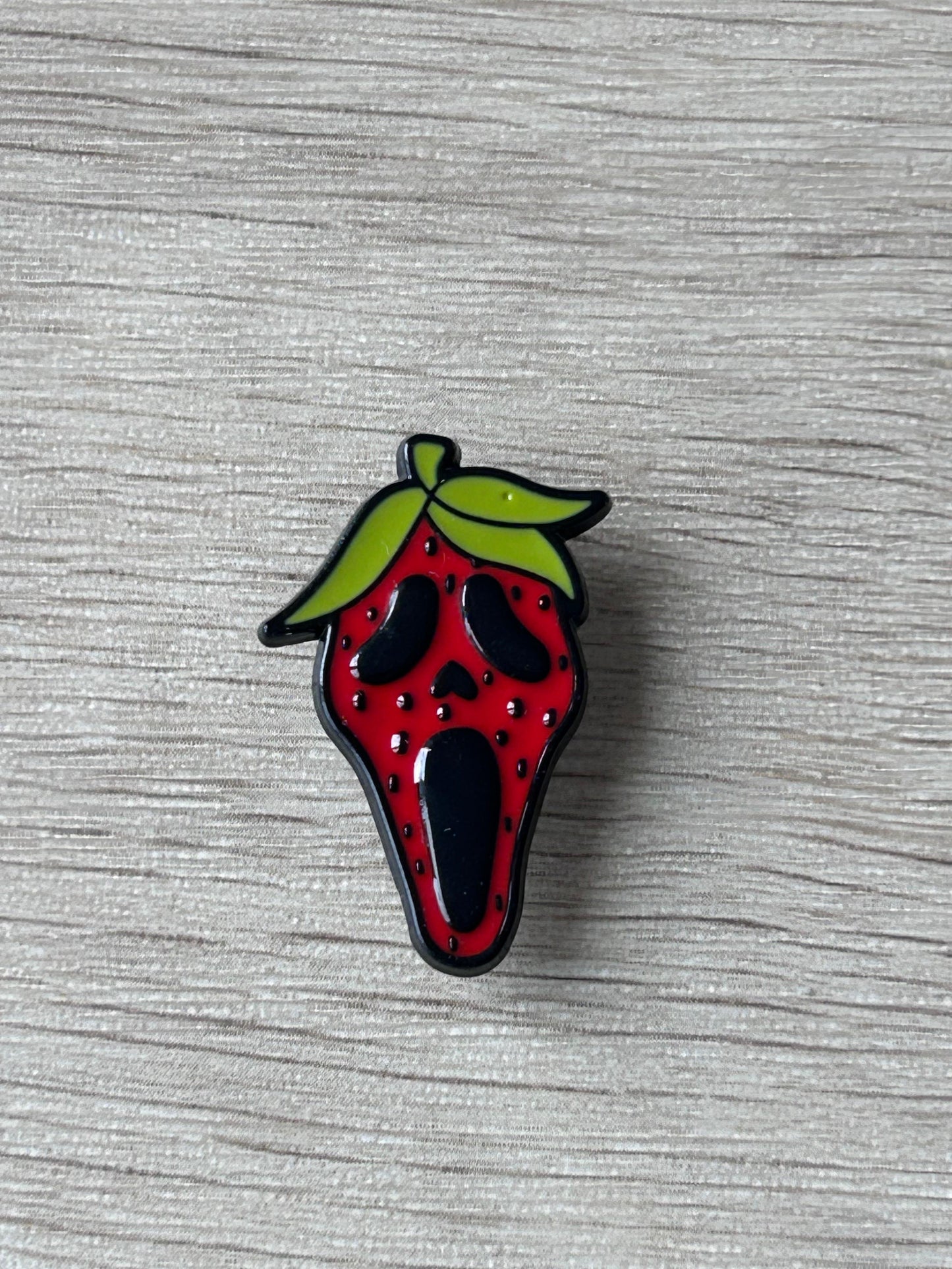 Épingle en forme de fraise rouge, feuilles vertes, détails noirs et points