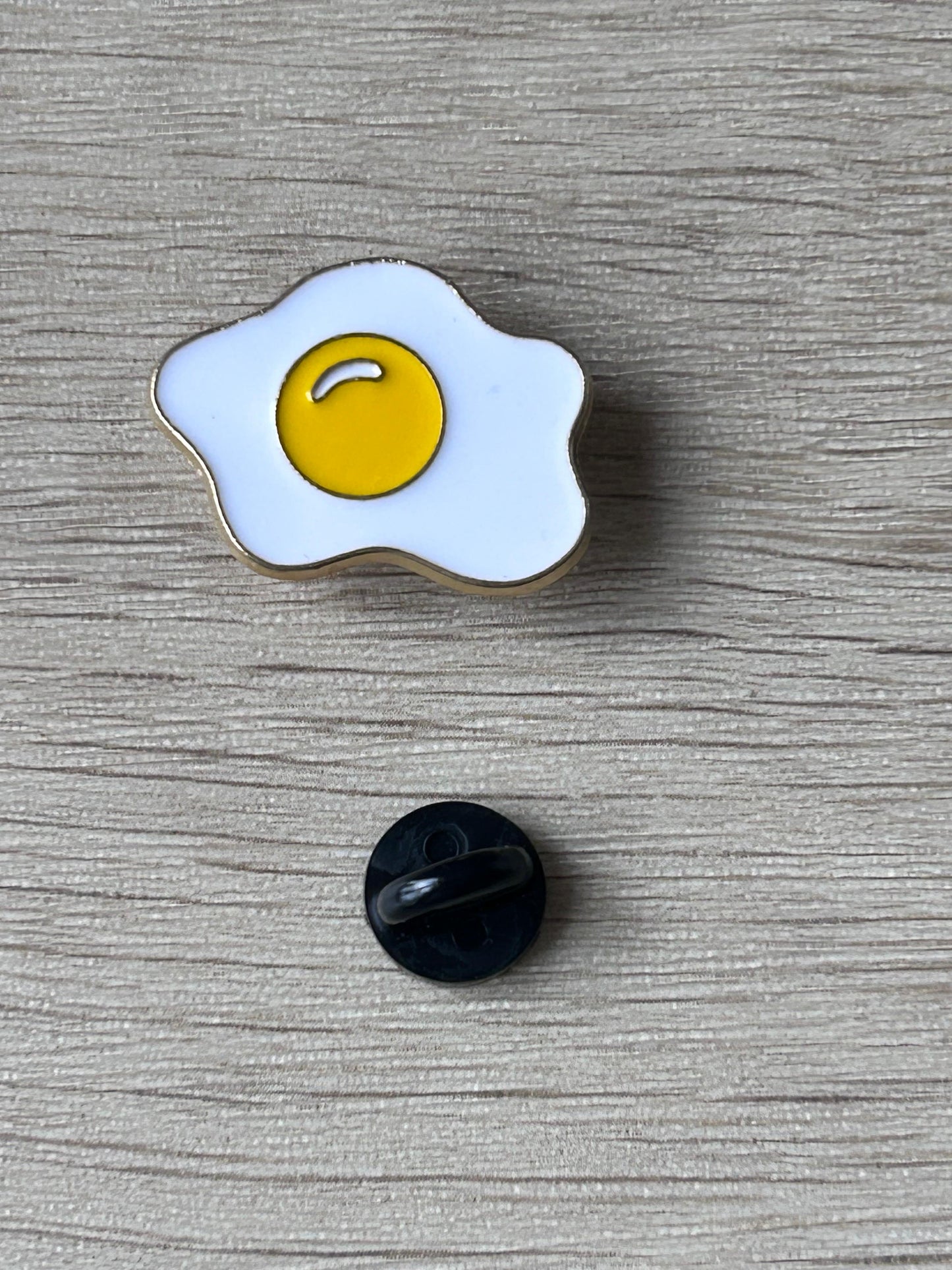 Pin œuf au plat émaillé jaune et blanc, avec fermoir noir au dos.