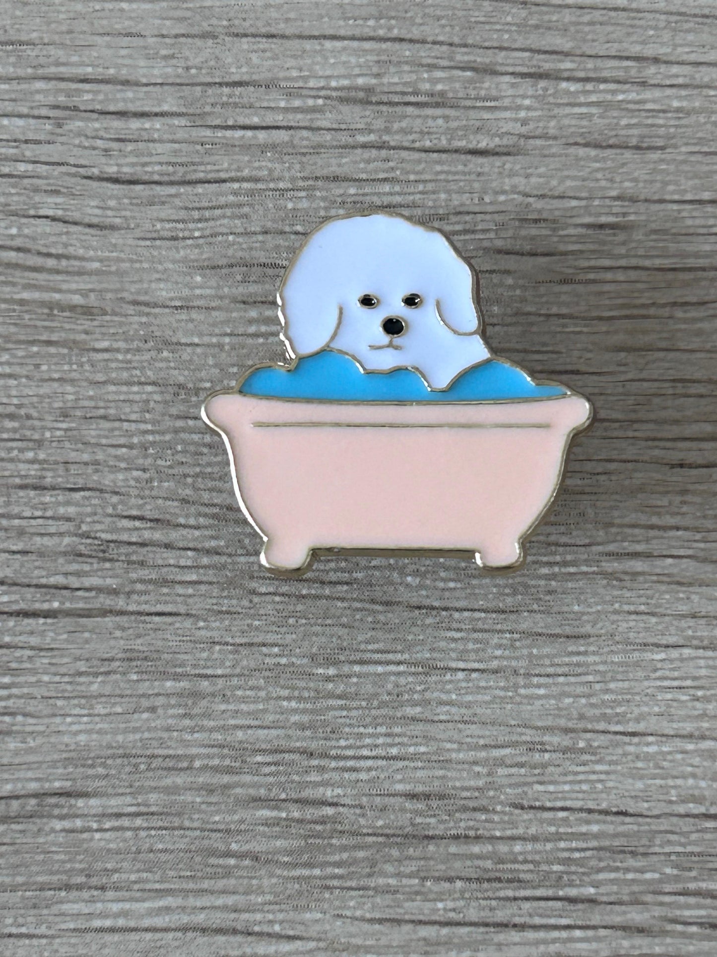 Pin's émaillé : chien blanc dans une baignoire rose et bleu, visage souriant.