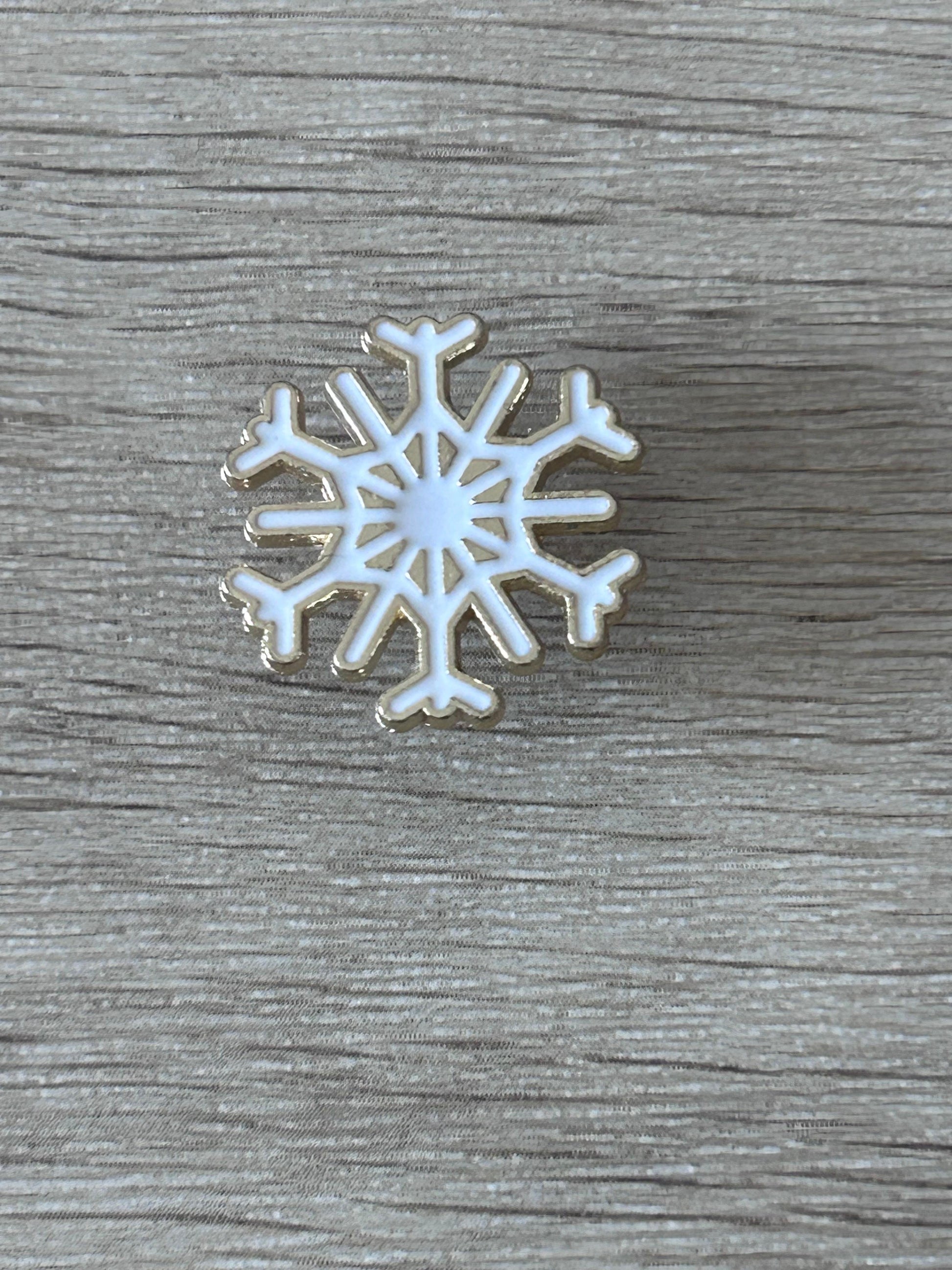 Broche flocon de neige argenté à centre blanc, motif ajouré et épingle métallique.
