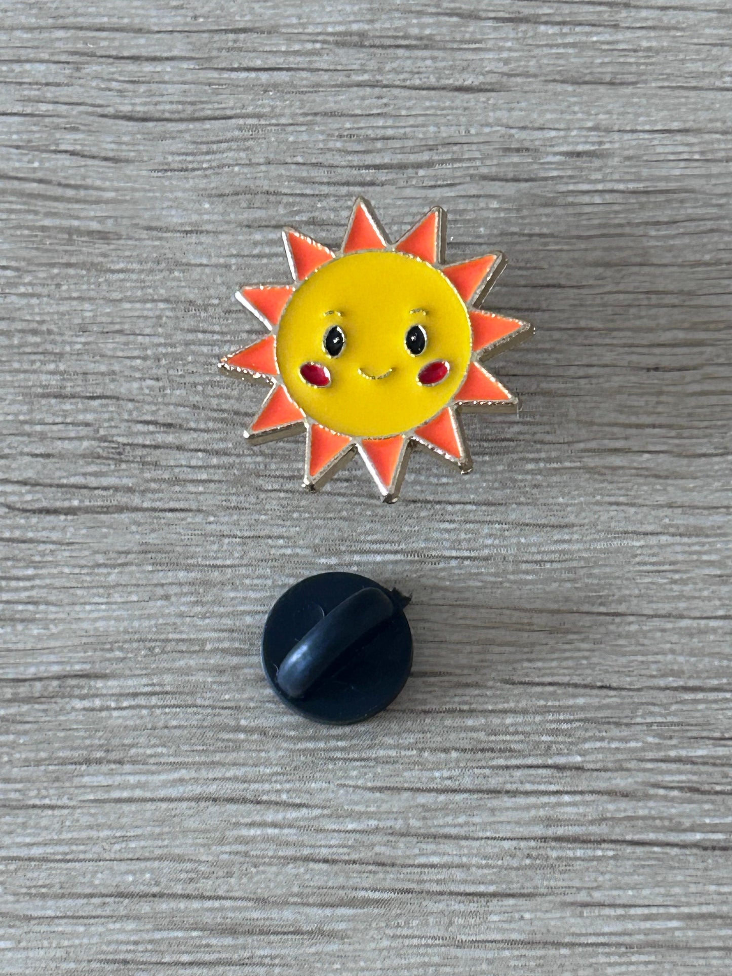 Épingle soleil souriant jaune à visage, contour orange, avec attache noire visible