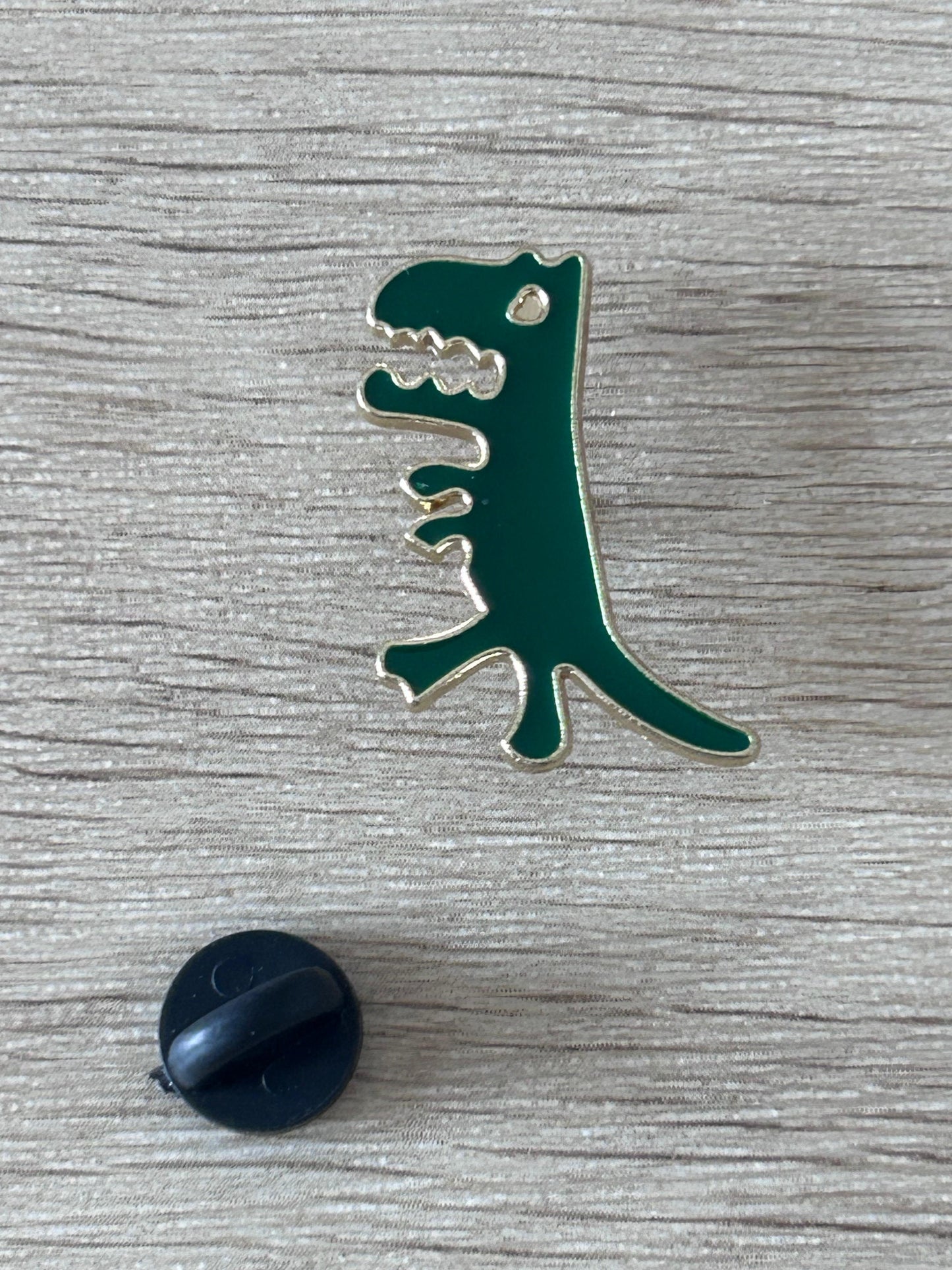 Broche T-Rex verte avec détails argentés et embout noir rond.
