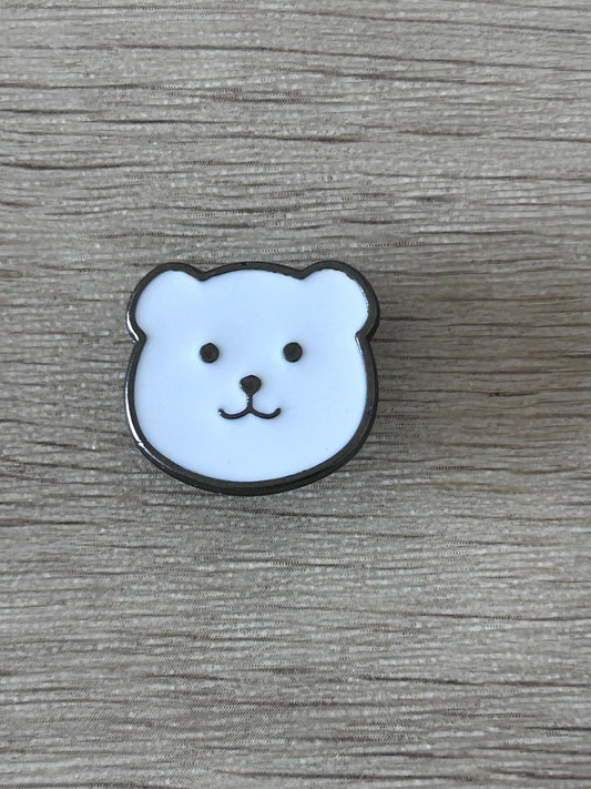 Épingle en forme de tête d’ours bleu clair, sourire et contour noir.