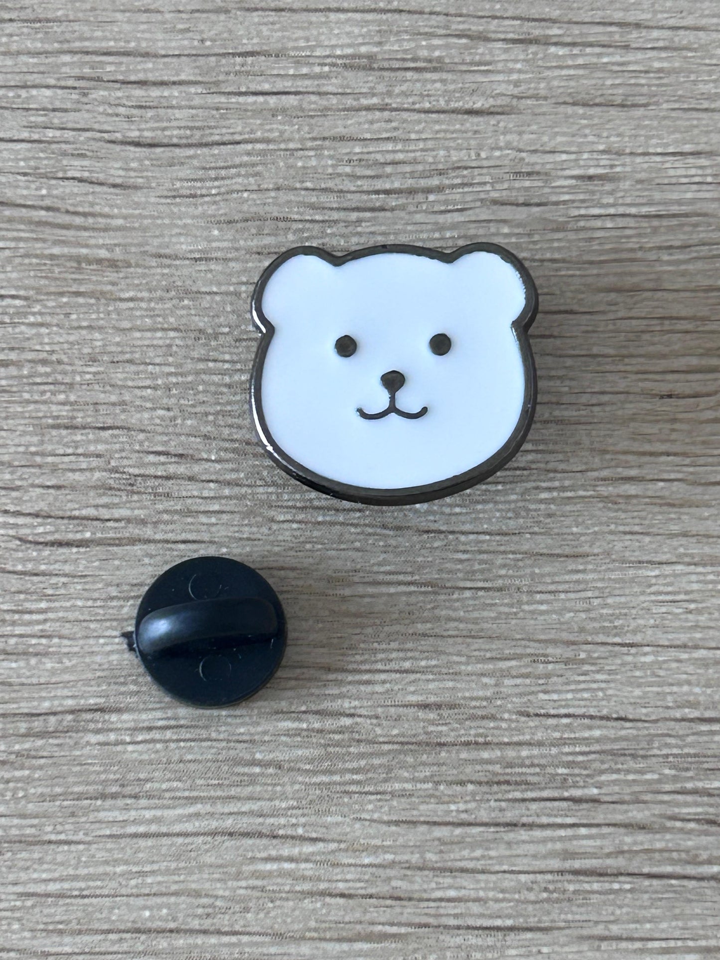 Épingle en forme de tête d’ours bleu clair, contour noir, avec dos noir.