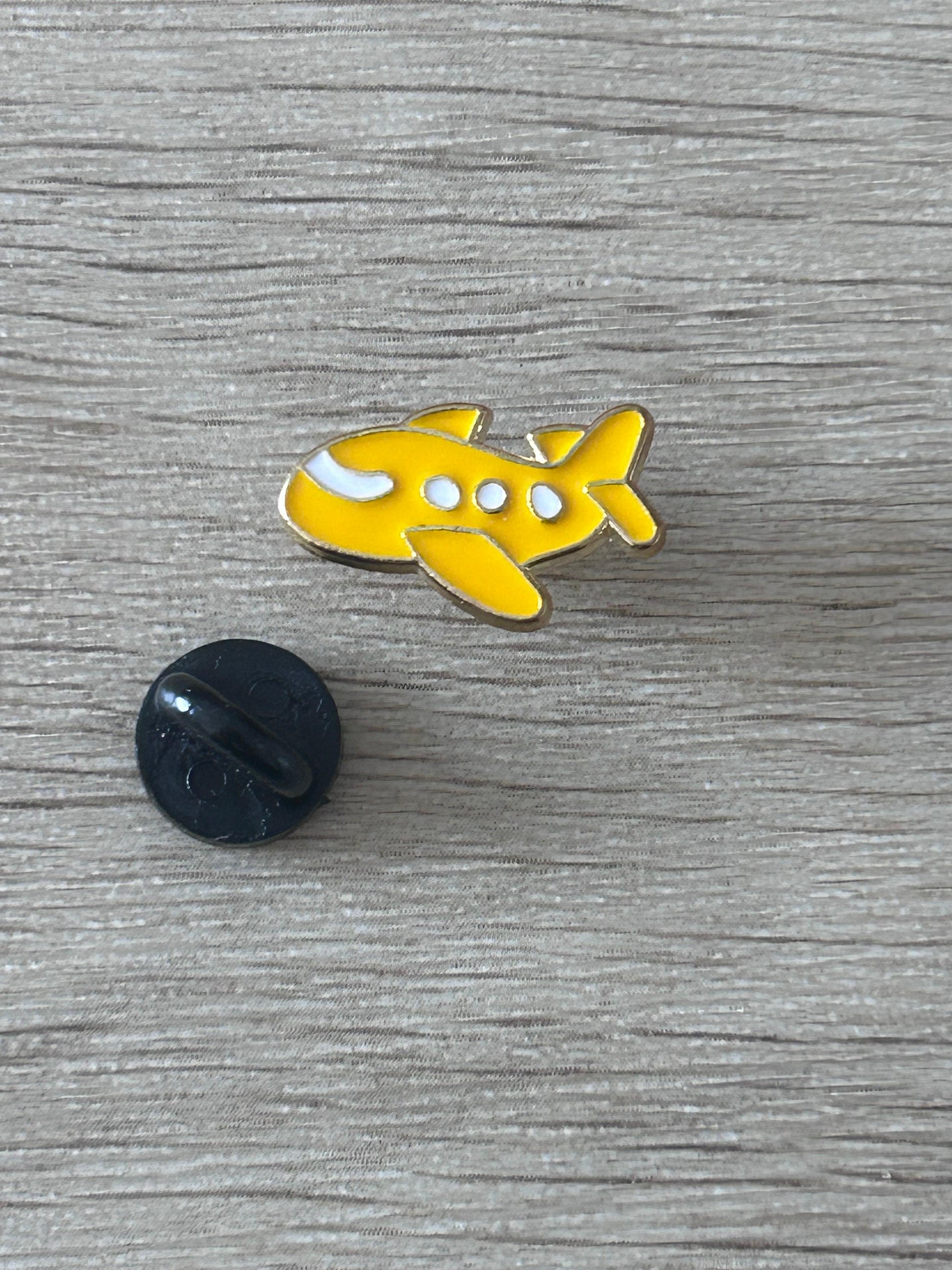 Broche avion jaune kawaii en métal avec attache noire, émail blanc.